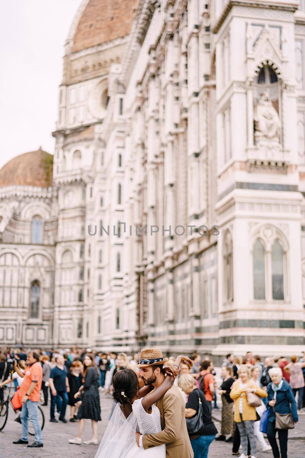 African-American bride and Caucasian groom kissing among the crowd in Piazza del Duomo. Wedding in Florence, Italy. Mixed-race wedding couple