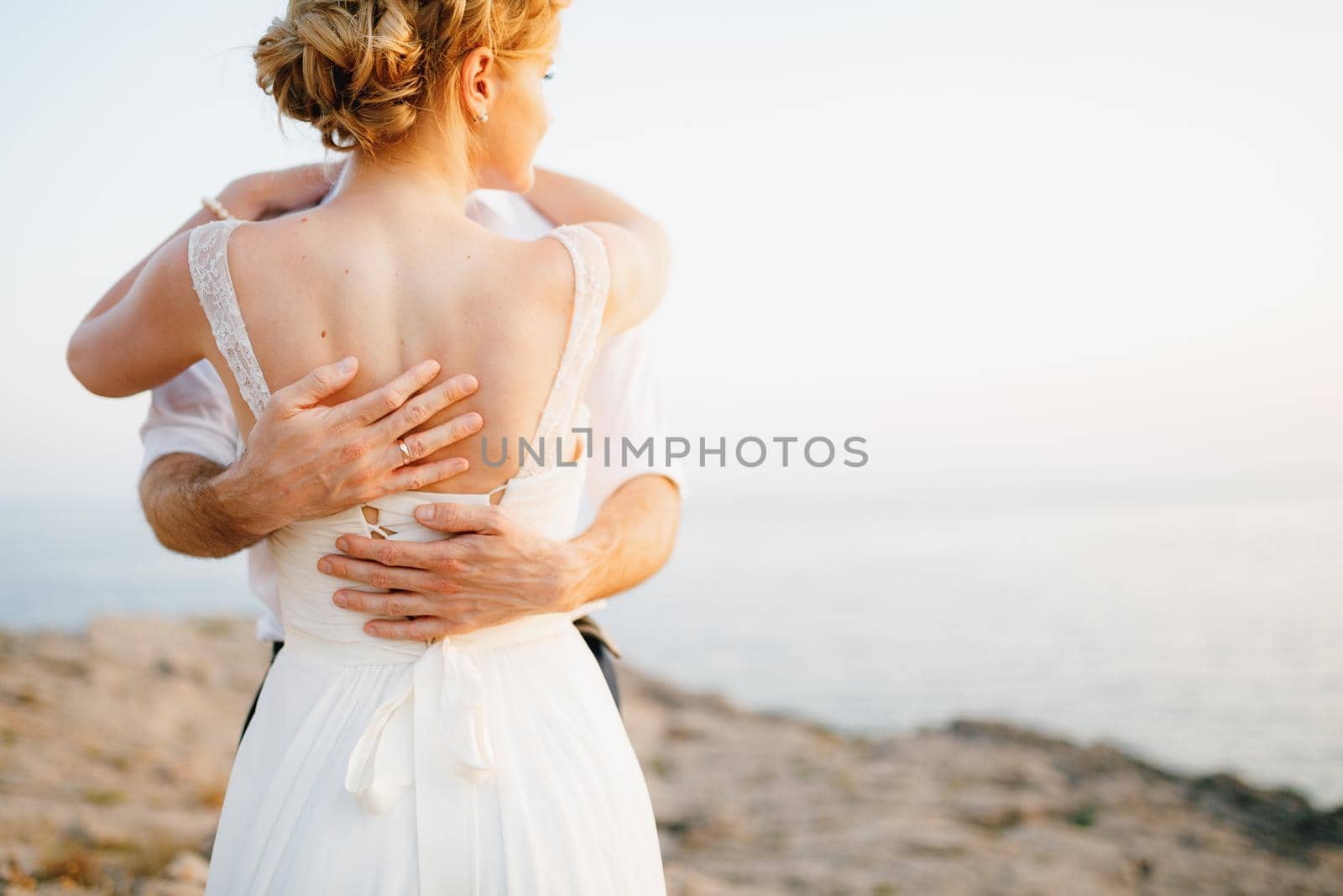 The bride and groom hug on the rocks by the sea against the backdrop of the mountains and the island of Mamula, back view. High quality photo