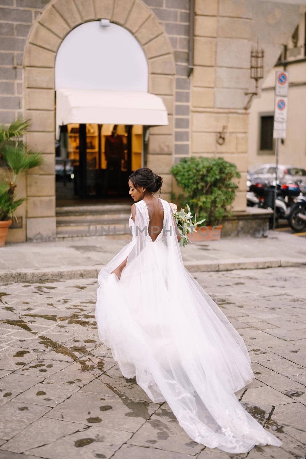 African-American bride in a white dress with a long veil and bouquet in hand. Wedding in Florence, Italy.