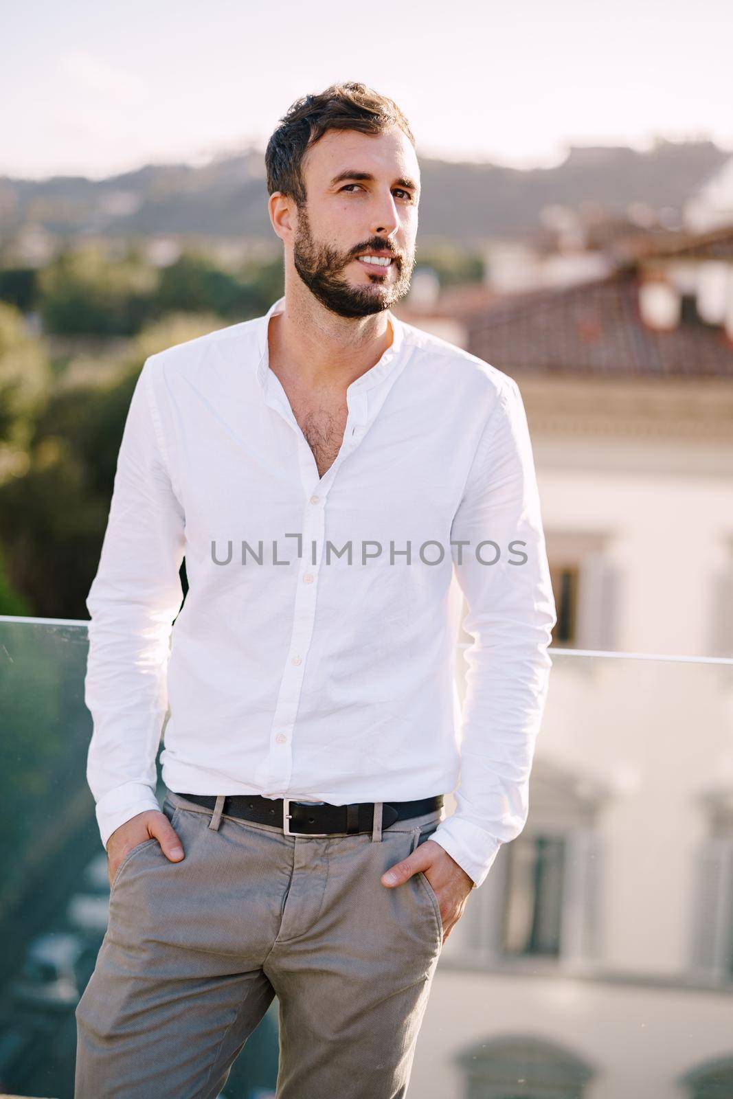 Stylish bearded guy in white shirt and light trousers on a rooftop terrace in Florence, Italy