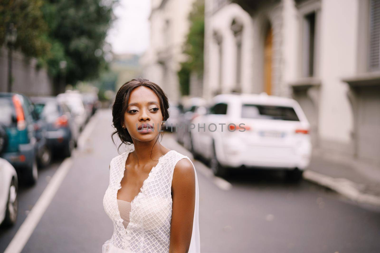 An African-American bride in a white dress, with a long veil, walks on the road on a city street. Wedding in Florence, Italy