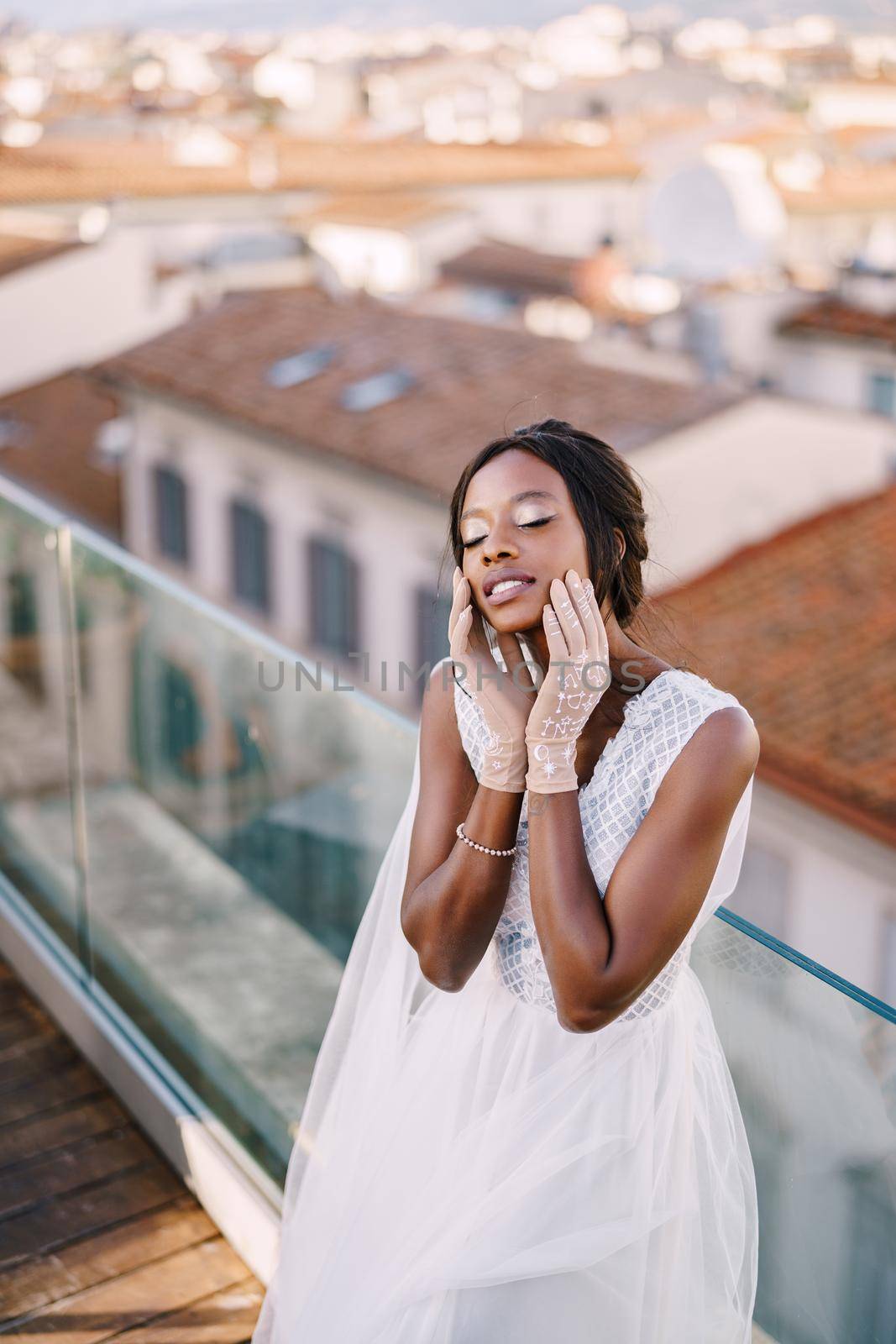 A beautiful African-American bride in white wedding dress, touches her face in vintage gloves. Fine-Art wedding in Florence, Italy