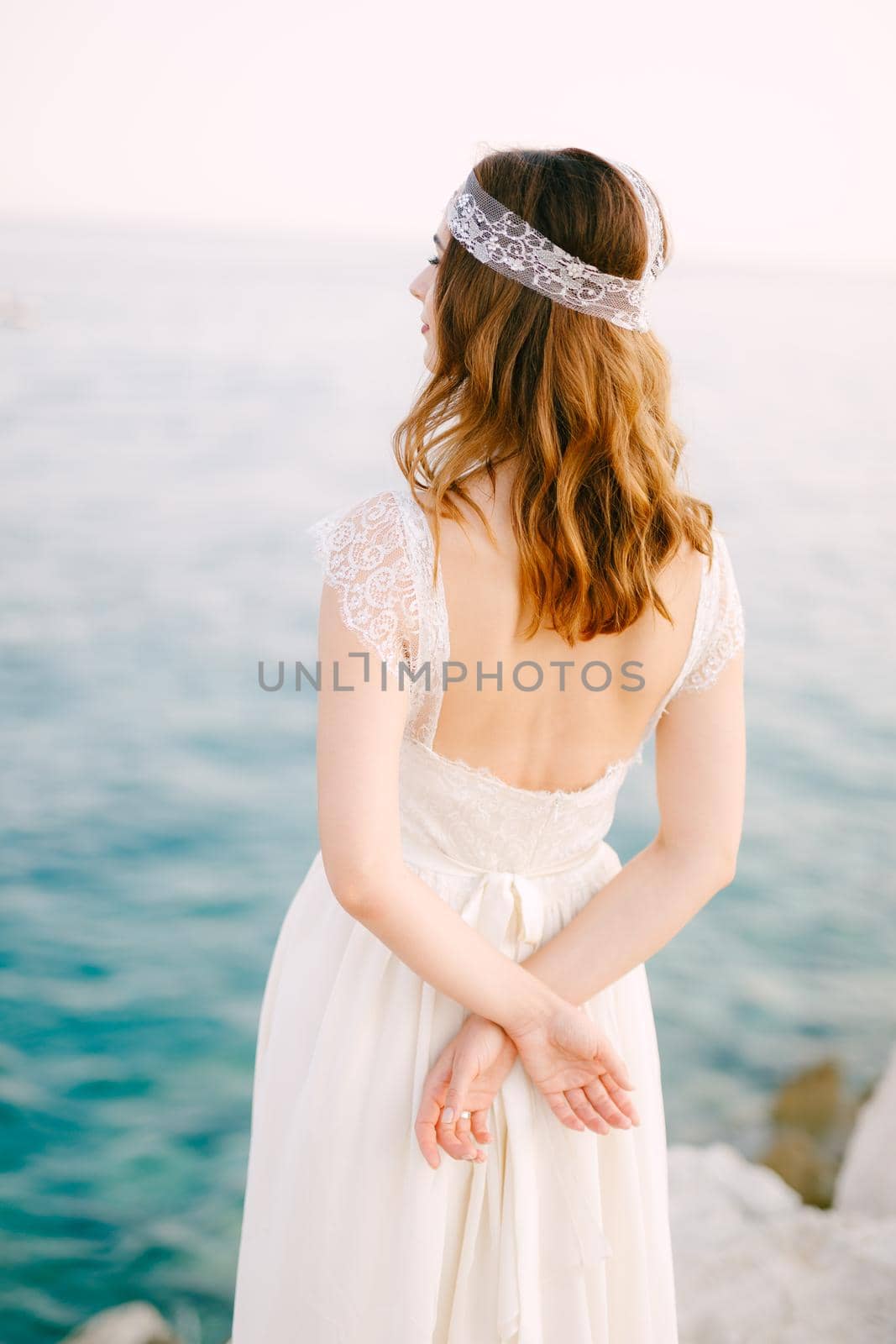 The bride stands on the seashore with her hands folded behind her back and looks into the distance. High quality photo