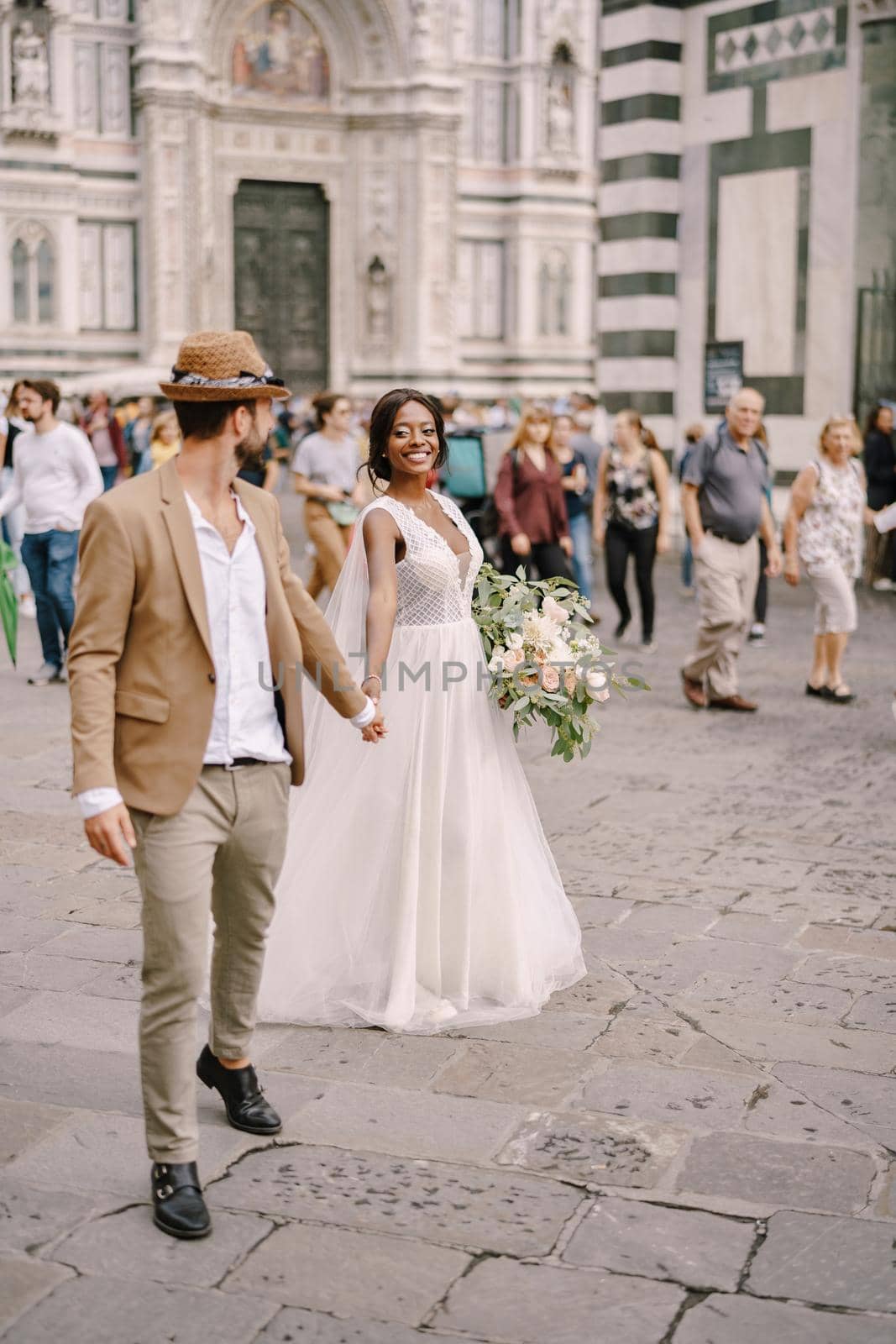 African-American bride and Caucasian groom walk along the Piazza del Duomo. Interracial wedding couple. Wedding in Florence, Italy
