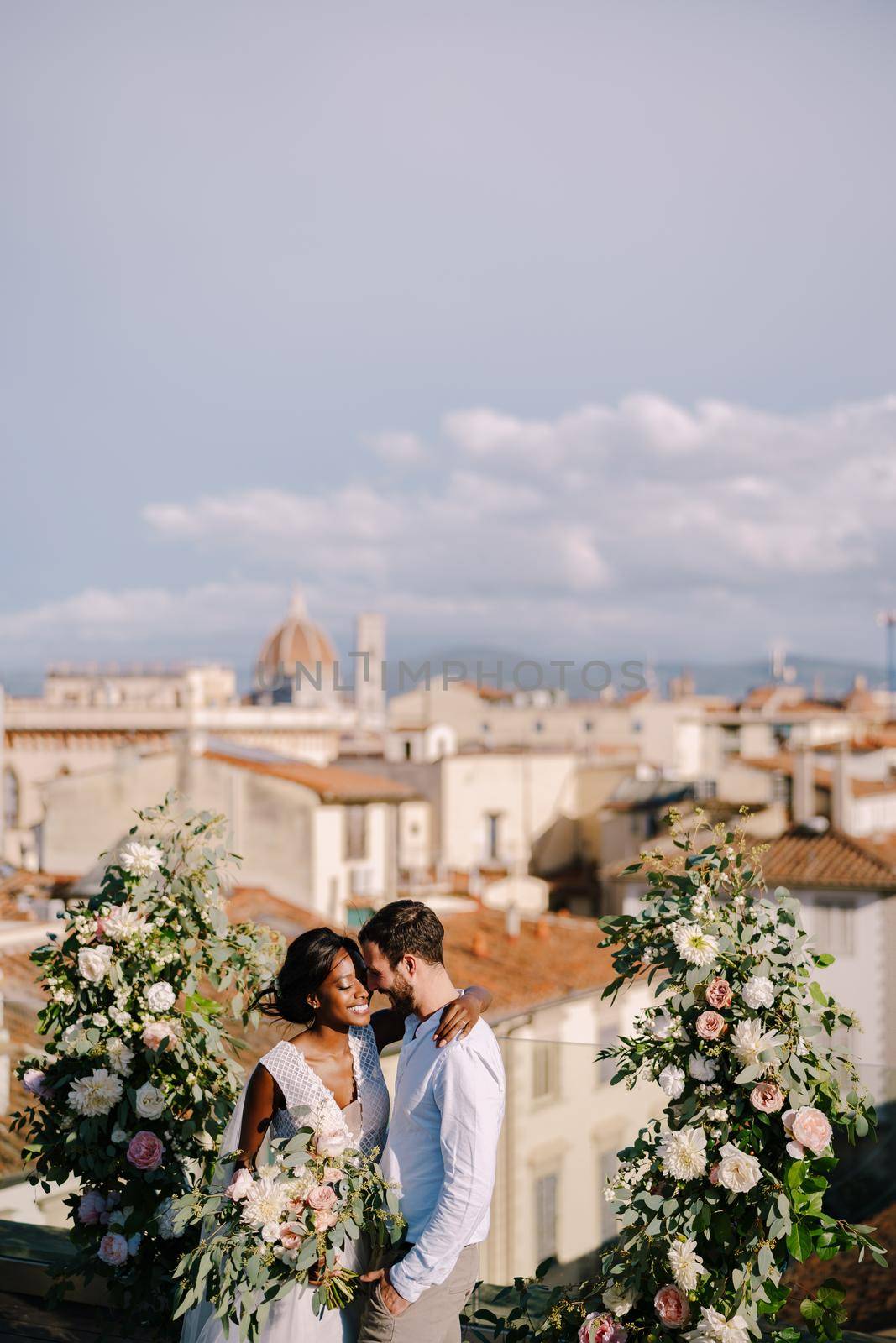 Interracial wedding couple. Destination fine-art wedding in Florence, Italy. A wedding ceremony on the roof of the building, with cityscape views of the city and the Cathedral of Santa Maria Del Fiore by Nadtochiy