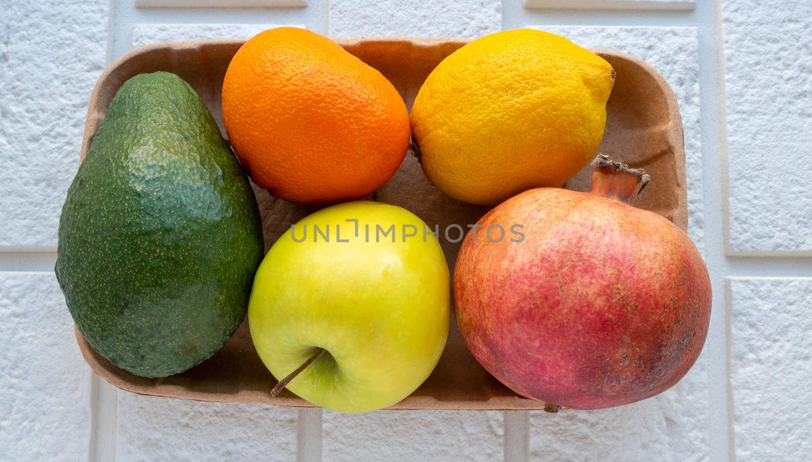 A small collection of fresh fruits in eco-friendly packaging on a white brick background.
