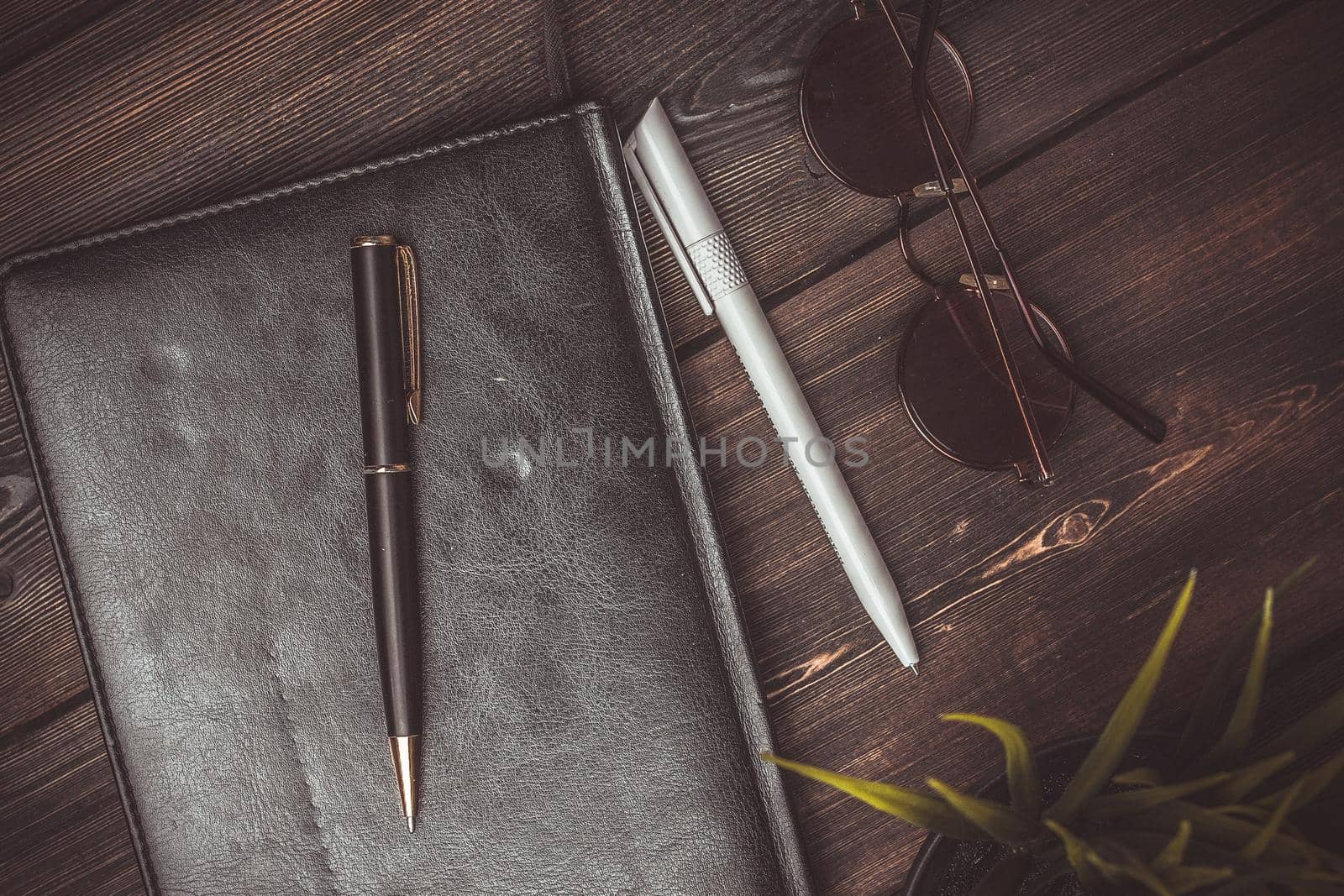 book with black cover and lies on a wooden table and a pen pencil jobs glasses flower potted coffee cup. High quality photo
