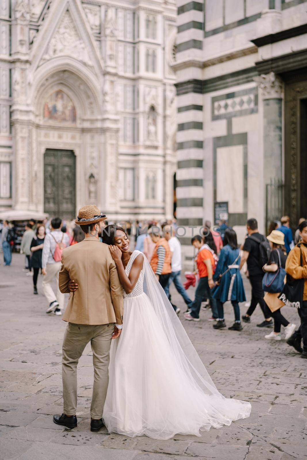 Mixed-race wedding couple. Wedding in Florence, Italy. African-American bride and Caucasian groom cuddling in Piazza del Duomo. by Nadtochiy