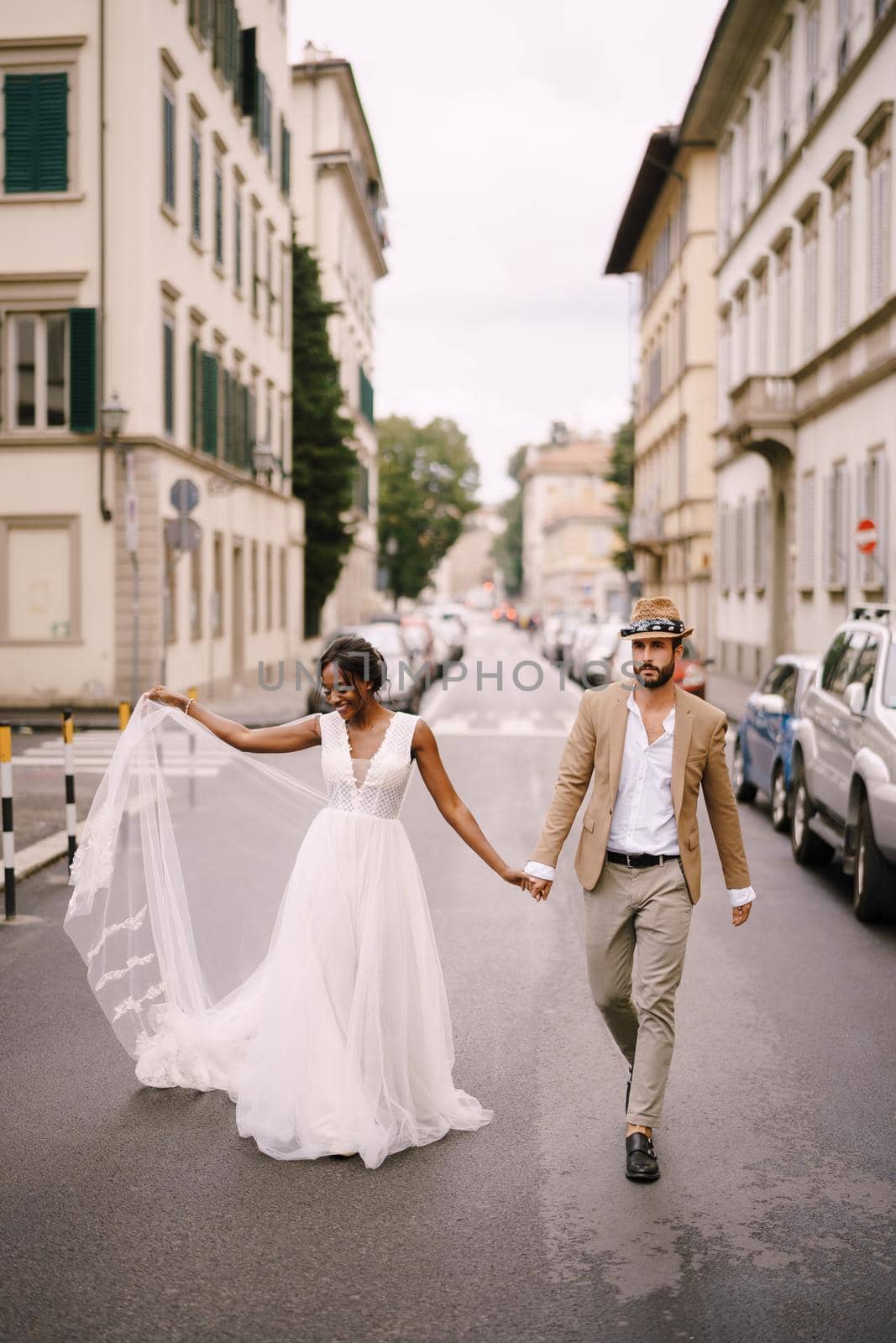 Wedding in Florence, Italy. Interracial wedding couple. African-American bride and Caucasian groom walk along the road among cars.