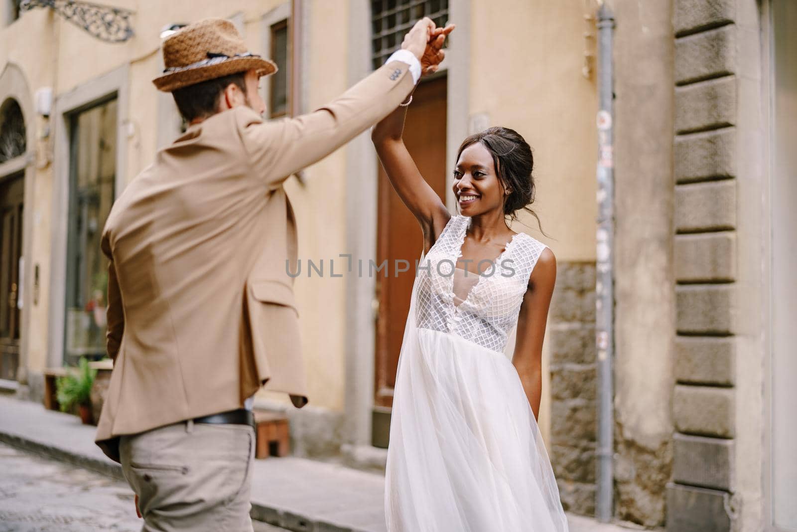 Interracial wedding couple. Wedding in Florence, Italy. African-American bride and Caucasian groom are dancing on the street. by Nadtochiy