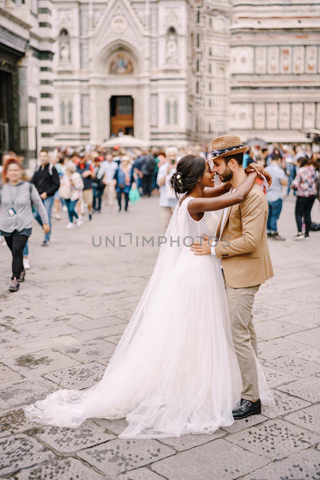 Interracial wedding couple. Wedding in Florence, Italy. African-American bride and Caucasian groom cuddling in Piazza del Duomo. by Nadtochiy