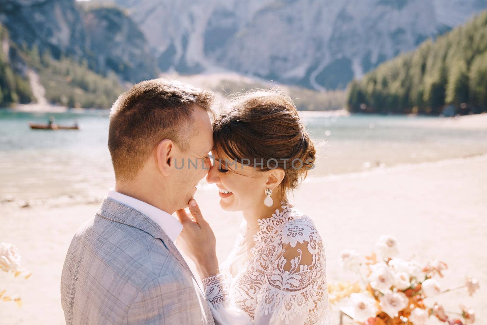 Newlyweds kiss on the spot for the ceremony, with an arch of autumn flower columns, against the backdrop of Lago di Braies in Italy. Destination wedding in Europe, at Braies lake.