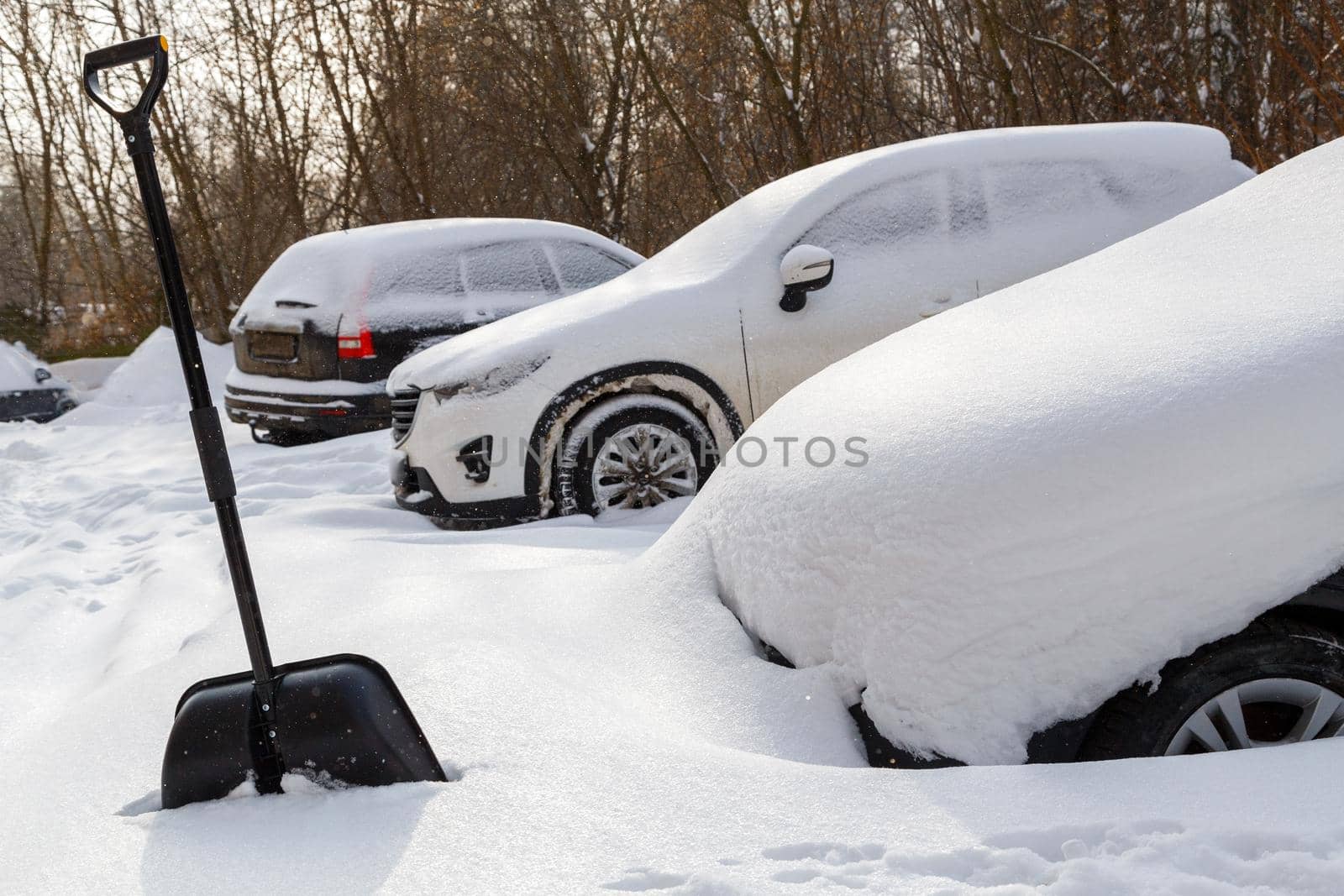 big black plastic shovel near snow covered cars at winter day light after heavy snowfall.