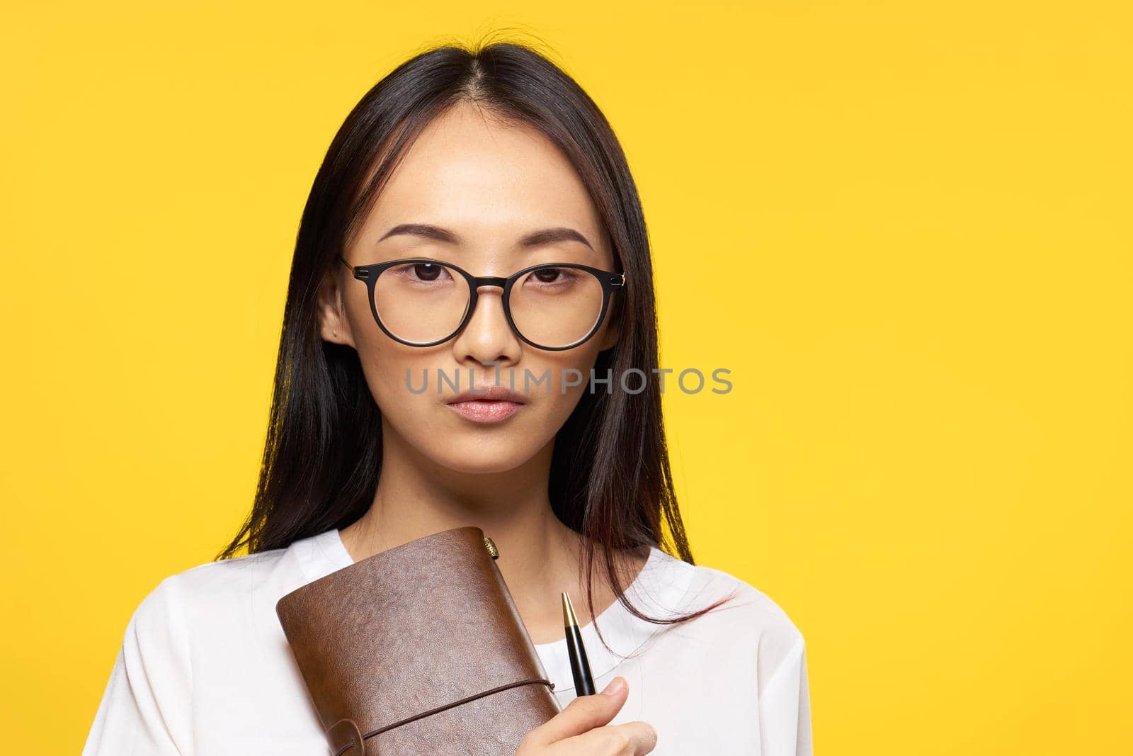 pretty brunette in white shirt holding notepad with pen office yellow background. High quality photo