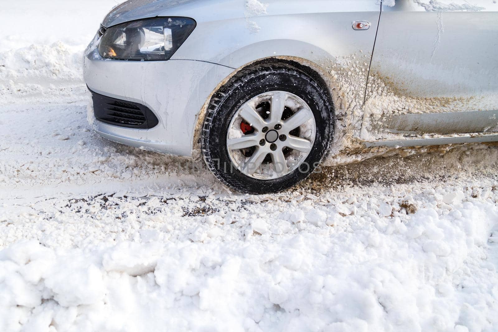 Silver vehicle moving on snowy road skidding, car's wheel spin and spew up pieces of snow it attempts to gain traction on the slippery surface.