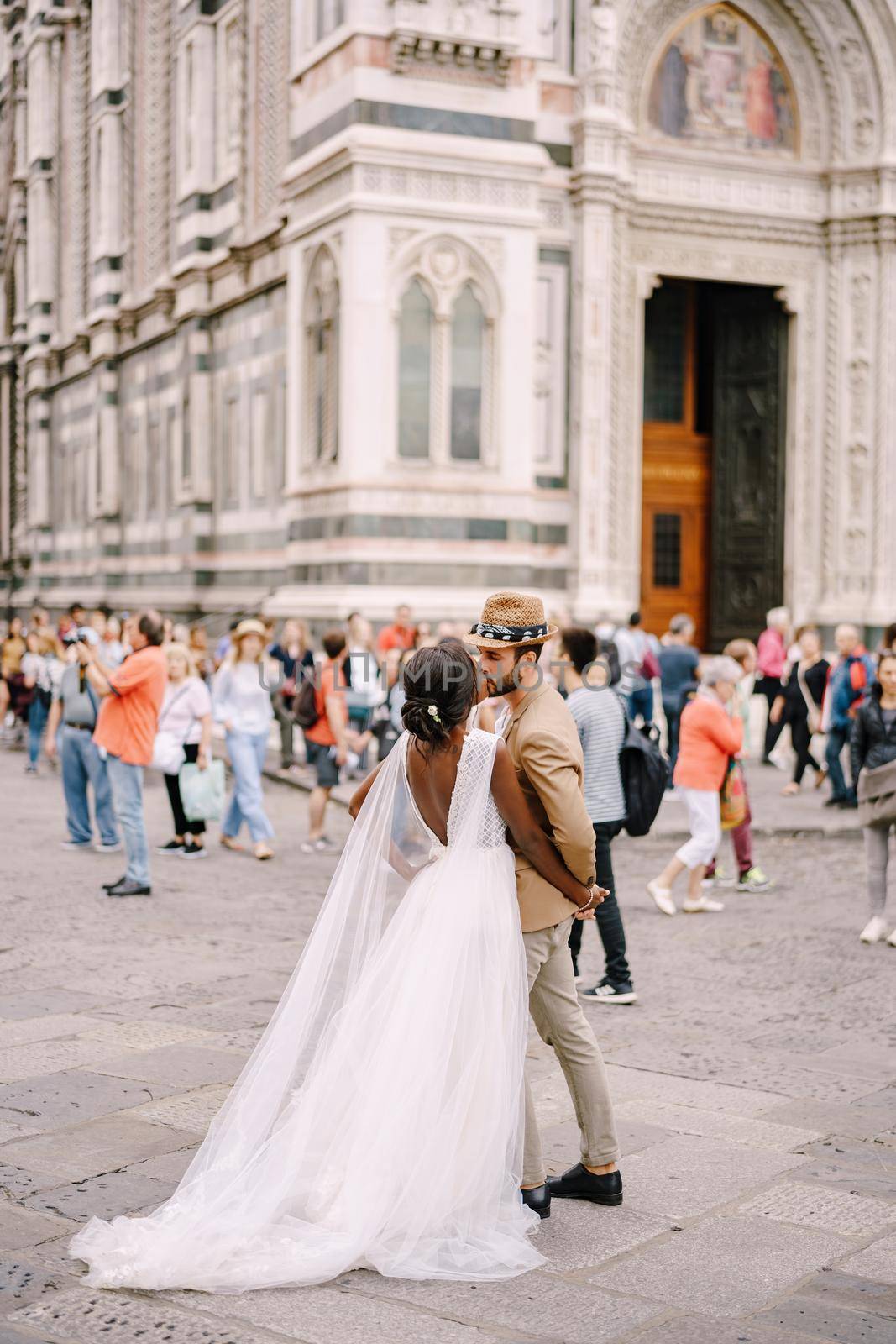 Interracial wedding couple. African-American bride and Caucasian groom kissing among the crowd in Piazza del Duomo. Wedding in Florence, Italy by Nadtochiy