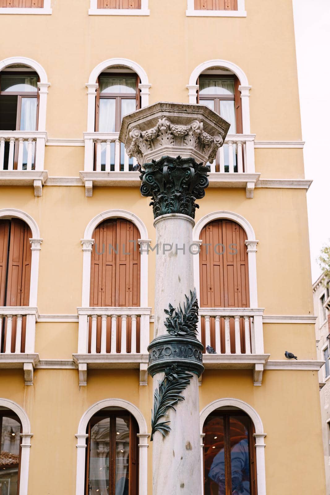 White column with an ornament against the background of a yellow building in Venice, Italy.