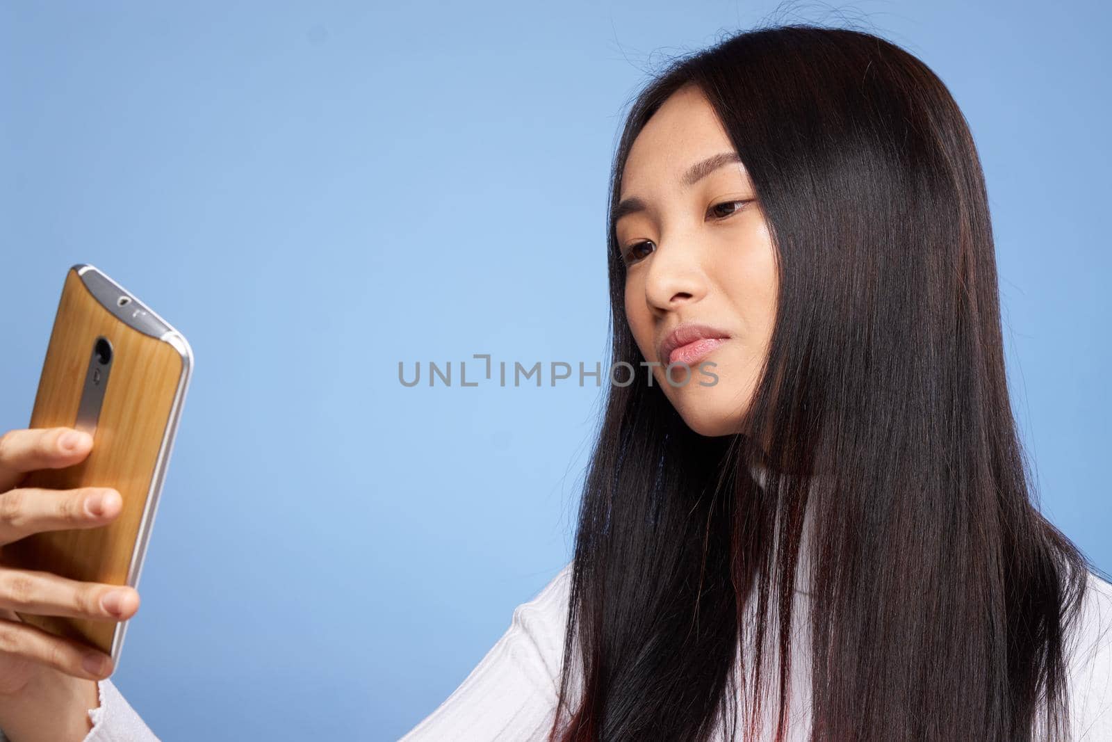 woman of asian appearance holding phone in hands internet communication technology blue background. High quality photo