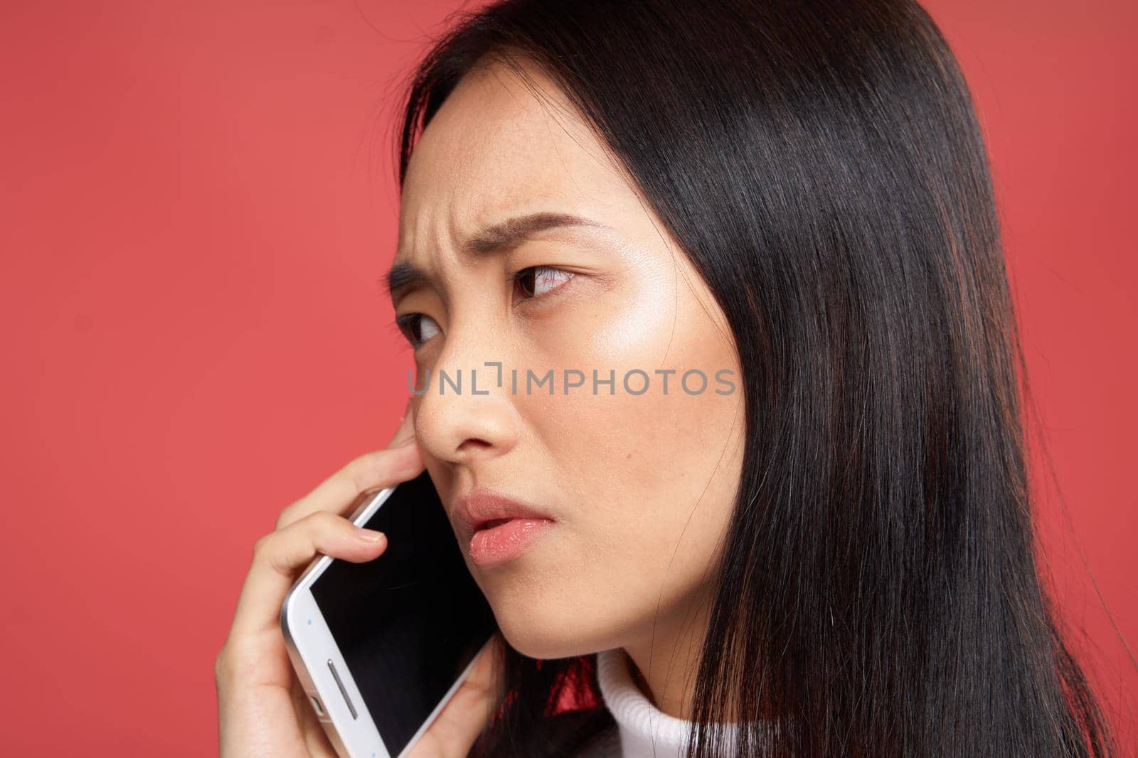 woman of asian appearance talking on the phone emotions dissatisfaction close-up red background. High quality photo