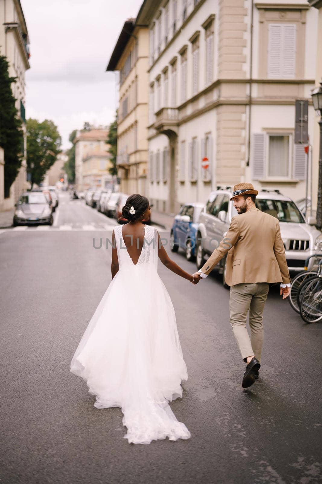 Wedding in Florence, Italy. Interracial wedding couple. African-American bride and Caucasian groom walk along the road among cars.