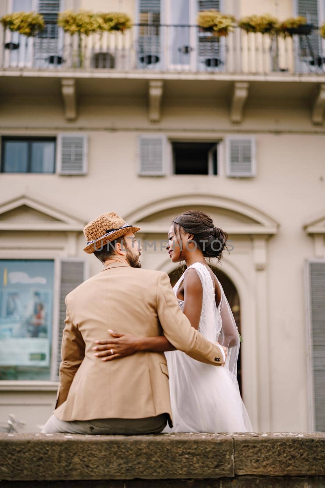 African-American bride in a white dress with a long veil and bouquet, and Caucasian groom in a sand jacket and straw hat. Interracial wedding couple. Wedding in Florence, Italy.