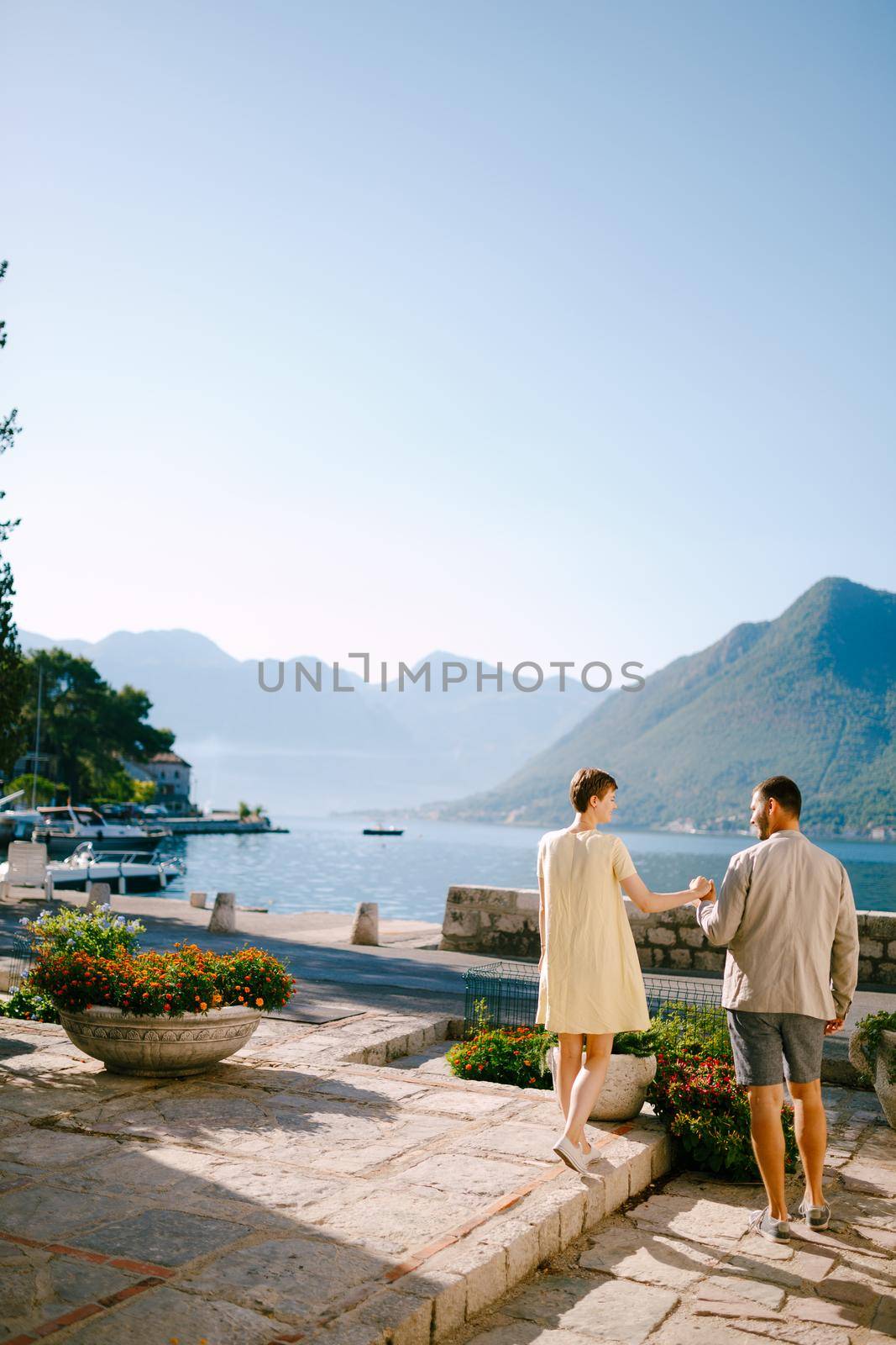 A man and a woman stand holding hands in Perast on the shore of the Bay of Kotor and look at each other . High quality photo