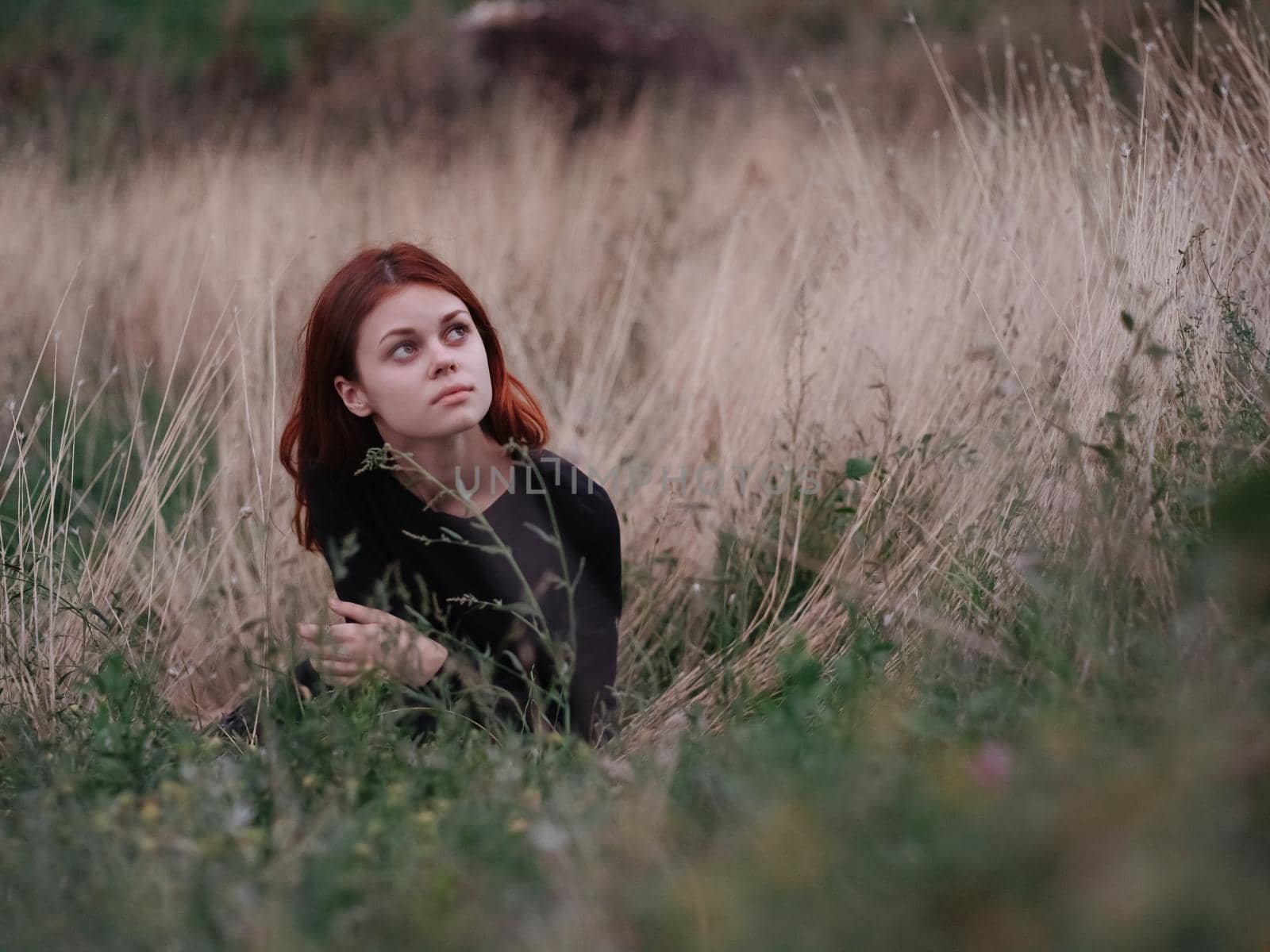red-haired woman in a black dress lies in a field on dry grass in nature by SHOTPRIME