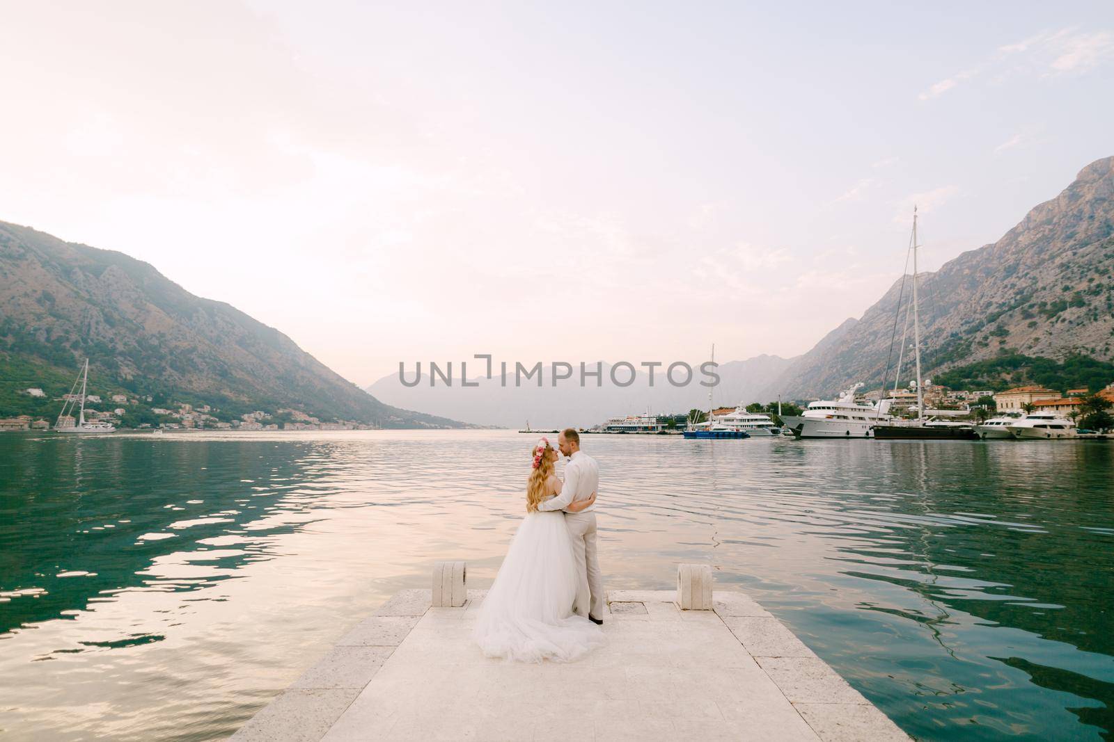 The bride in a wreath and groom hug on the pier near the old town of Kotor in the Bay of Kotor . High quality photo