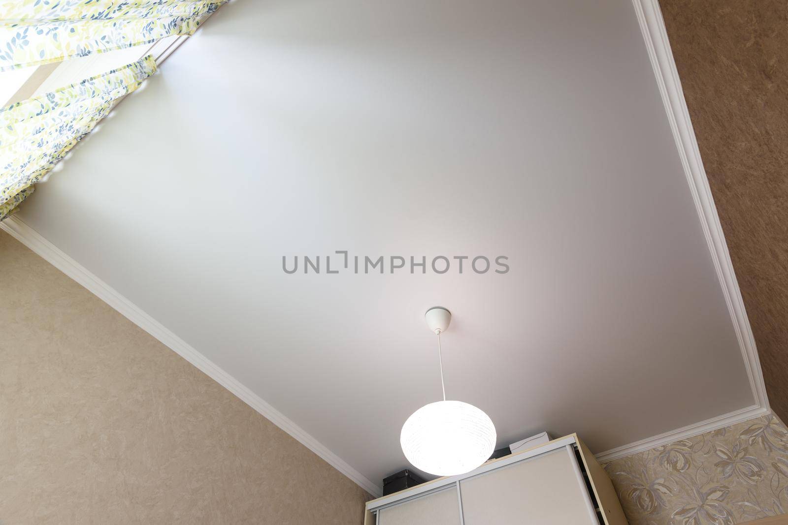 Stretch white matte ceiling close-up with a chandelier in the interior of a rectangular room by Madhourse