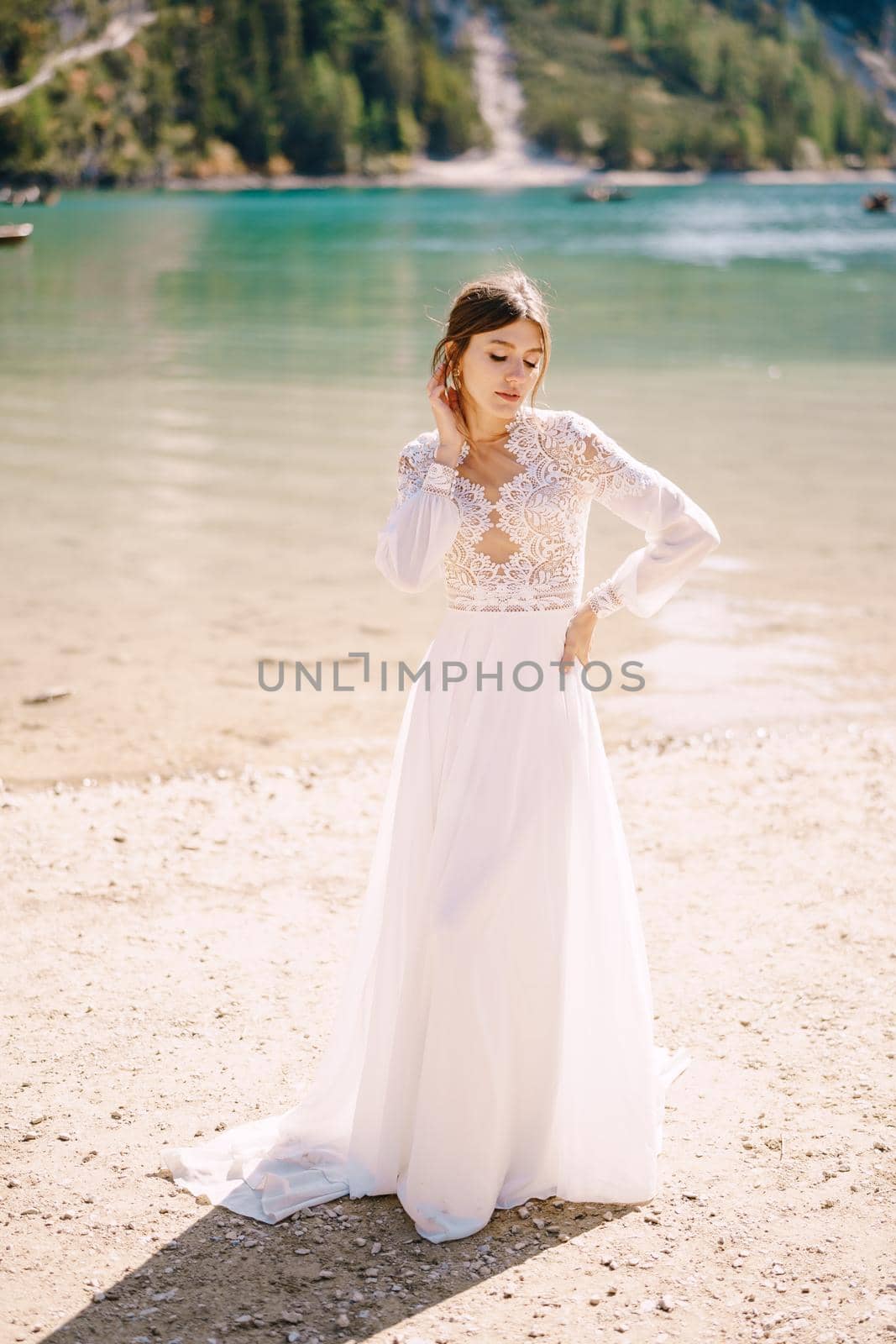 A beautiful bride in a white chiffon dress with sleeves and lace on the shores of Lake Lago di Braies in Italy. Destination wedding in Europe, on the popular Braies lake.