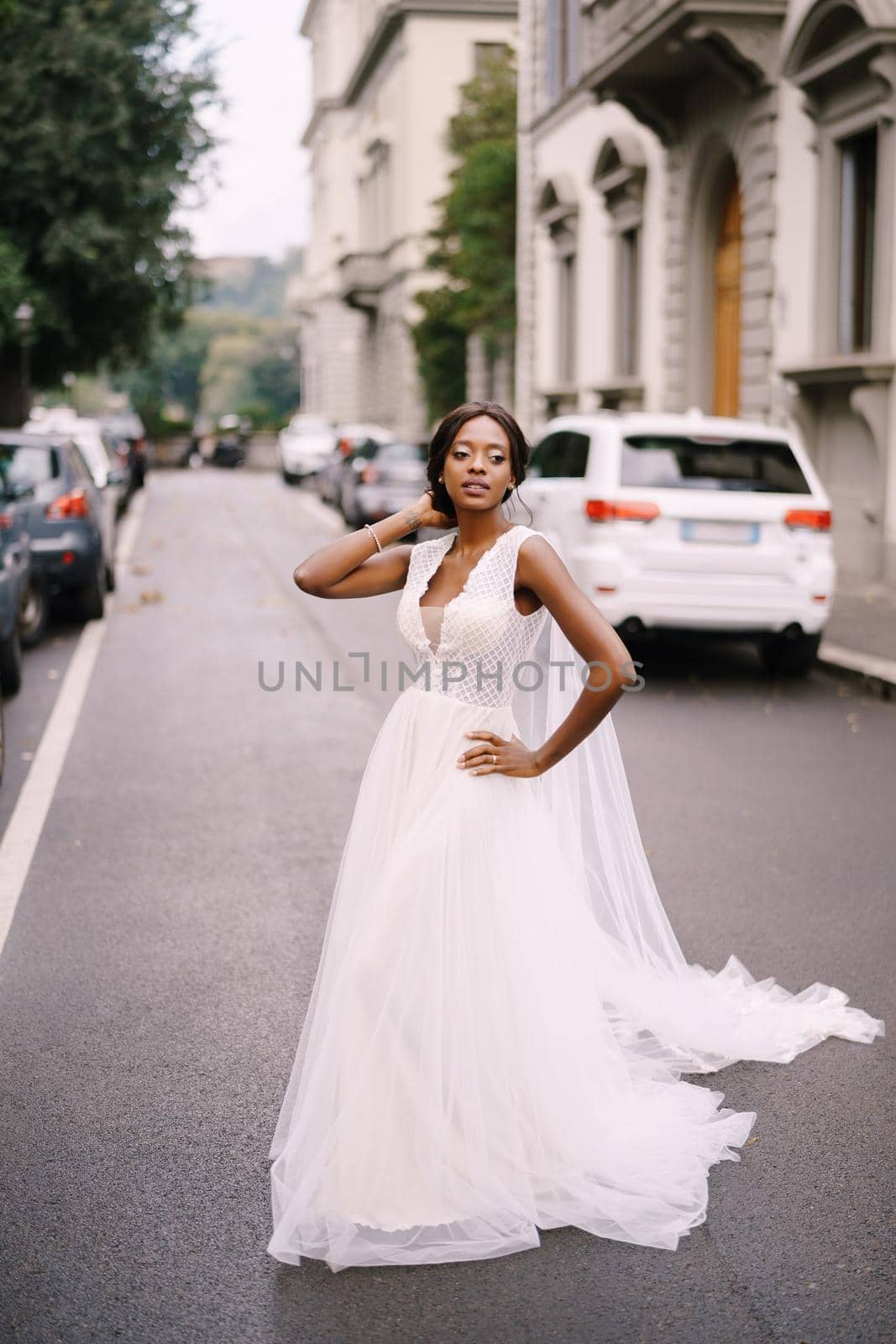 An African-American bride in a white dress, with a long veil, walks on the road on a city street. Wedding in Florence, Italy