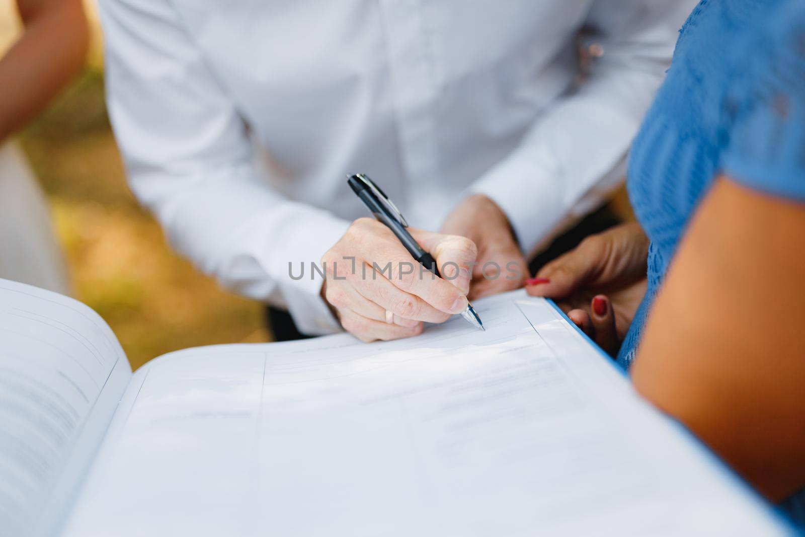 The groom signs the wedding certificate during the wedding ceremony, the bride stands near him, close-up. . High quality photo