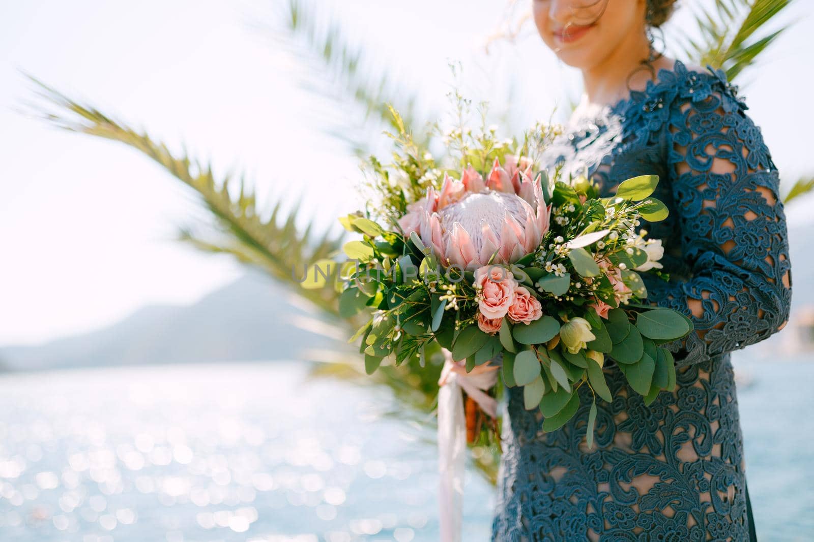 The bride in a stylish gray dress stands with wedding bouquets on the seashore, close-up. High quality photo
