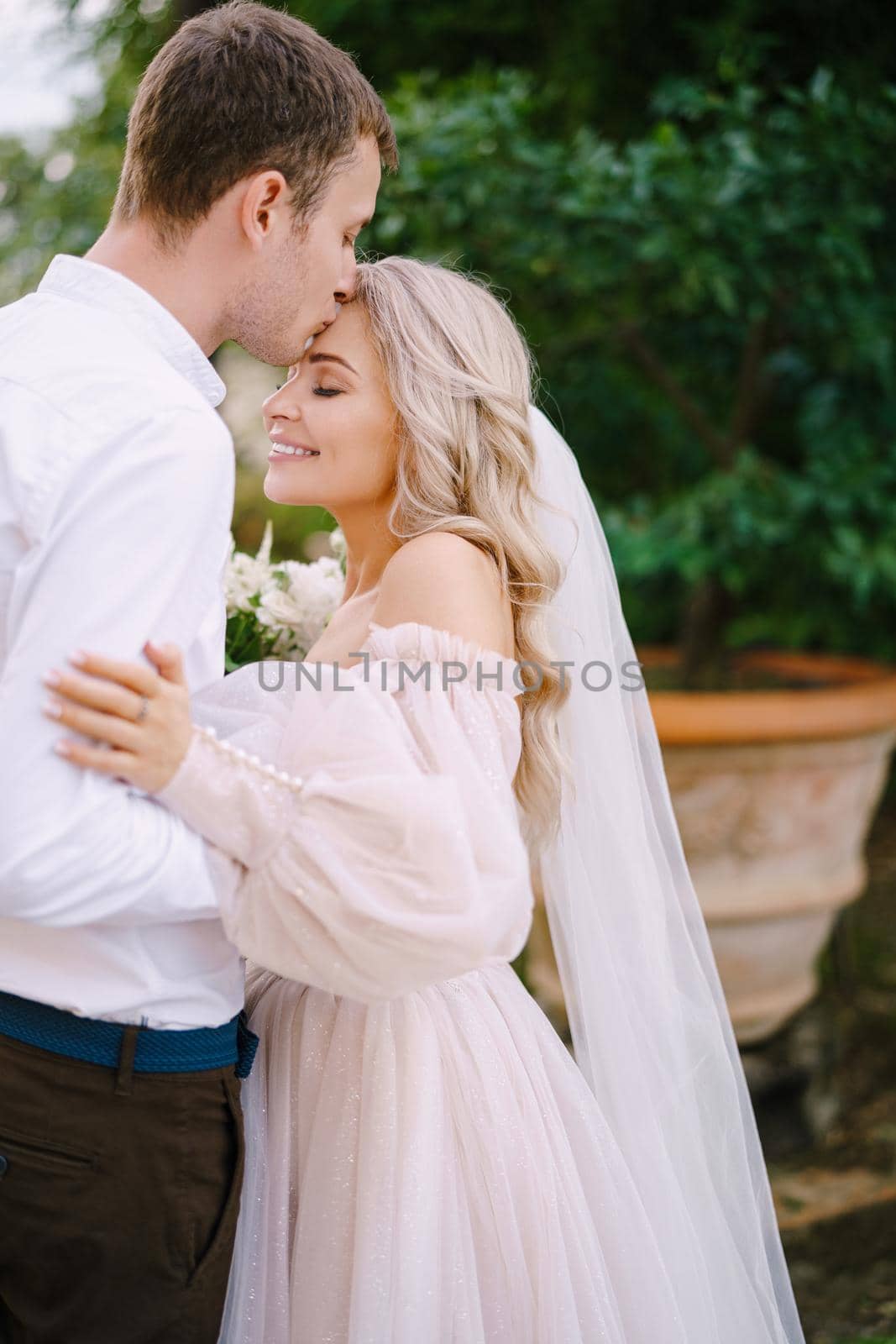 Wedding in Florence, Italy, in an old villa-winery. The groom kisses the bride on the forehead, close-up. by Nadtochiy