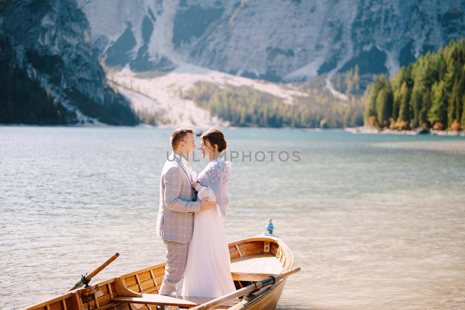 Bride and groom sailing in wooden boat, with oars at Lago di Braies lake in Italy. Wedding in Europe - Newlyweds are standing embracing in boat