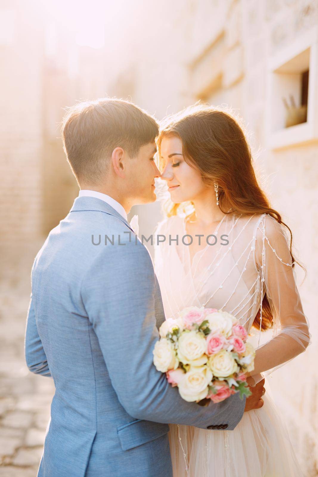 The bride and groom hug on a beautiful old street of Perast near a white stone wall, close-up. High quality photo