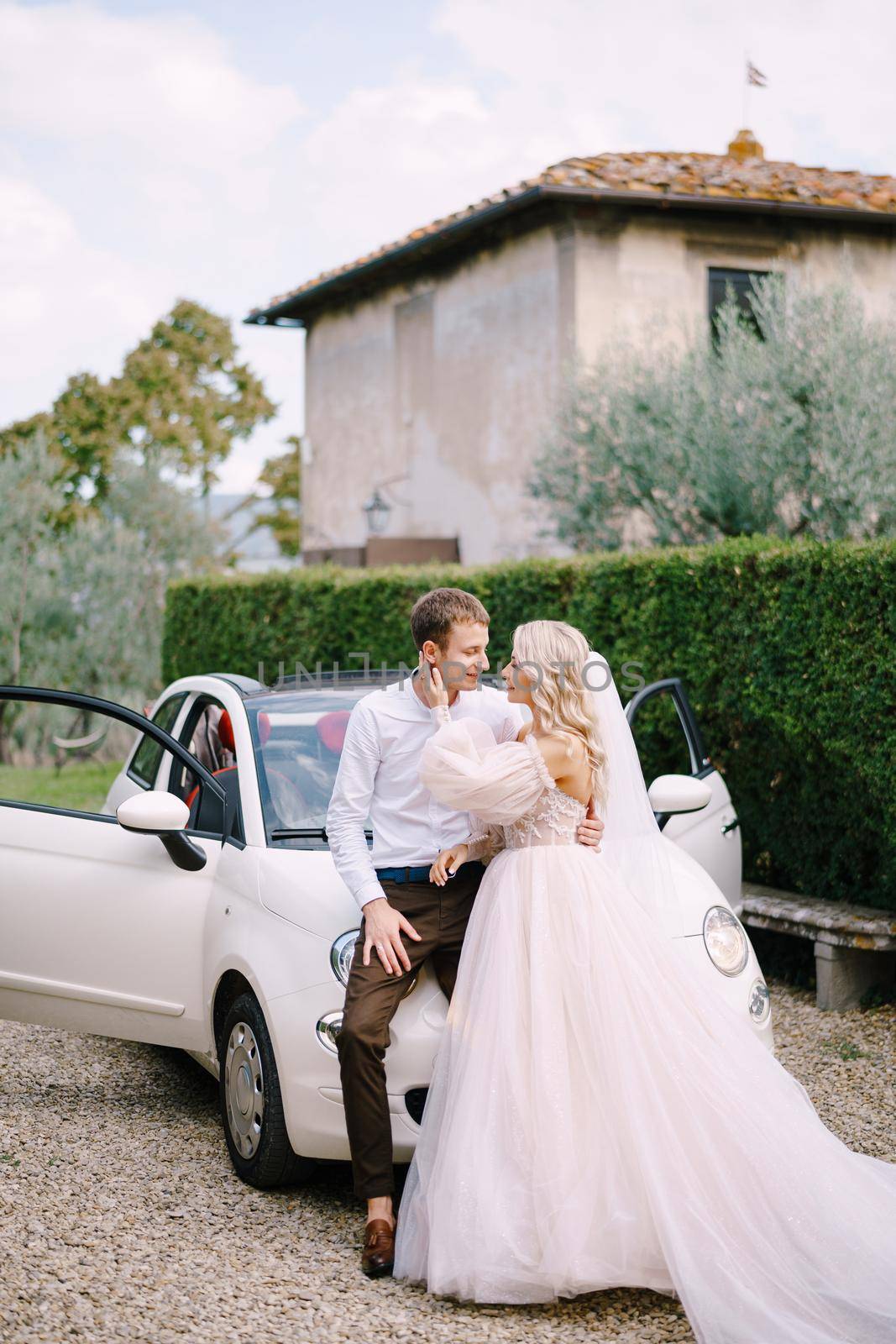 Beautiful bride and groom leaning on a convertible and looking at each other in front of the old villa in Italy, in Tuscany, near Florence