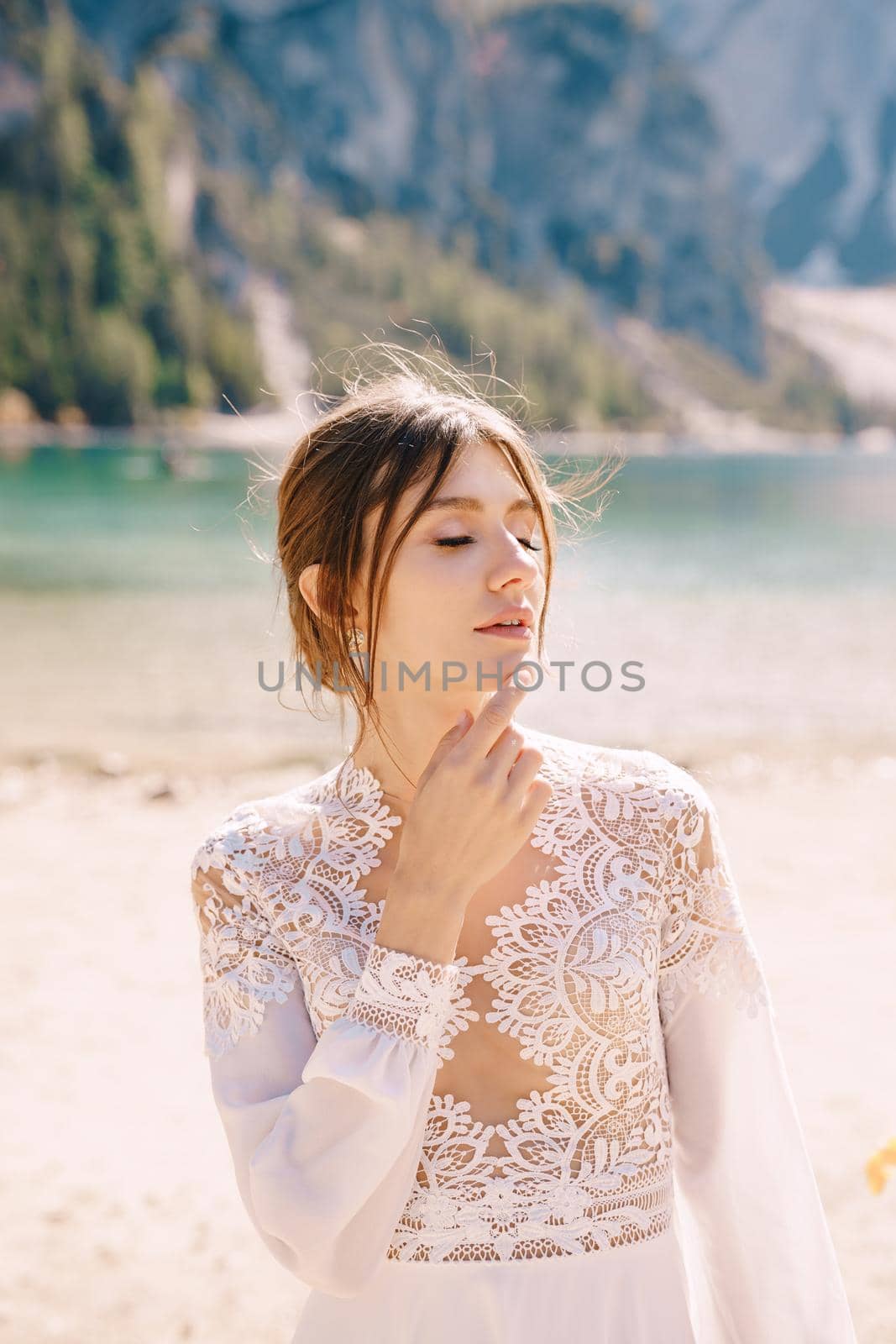 Beautiful bride in a white chiffon dress with sleeves and lace on the shore of Lake Lago di Braies in Italy. Destination wedding in Europe, on the popular Braies lake. by Nadtochiy