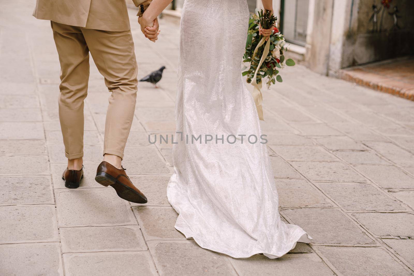 The bride and groom walk through the deserted streets of the city. Close-up of the newlyweds' feet and a long train of the bride's dress.