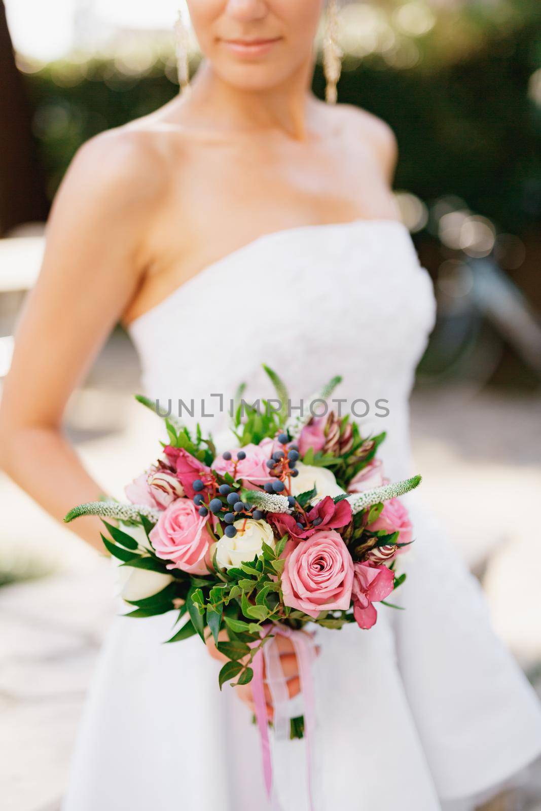 A sophisticated bride holding a wedding bouquet with roses, veronica, viburnum and boxwood in her hands, close-up . High quality photo