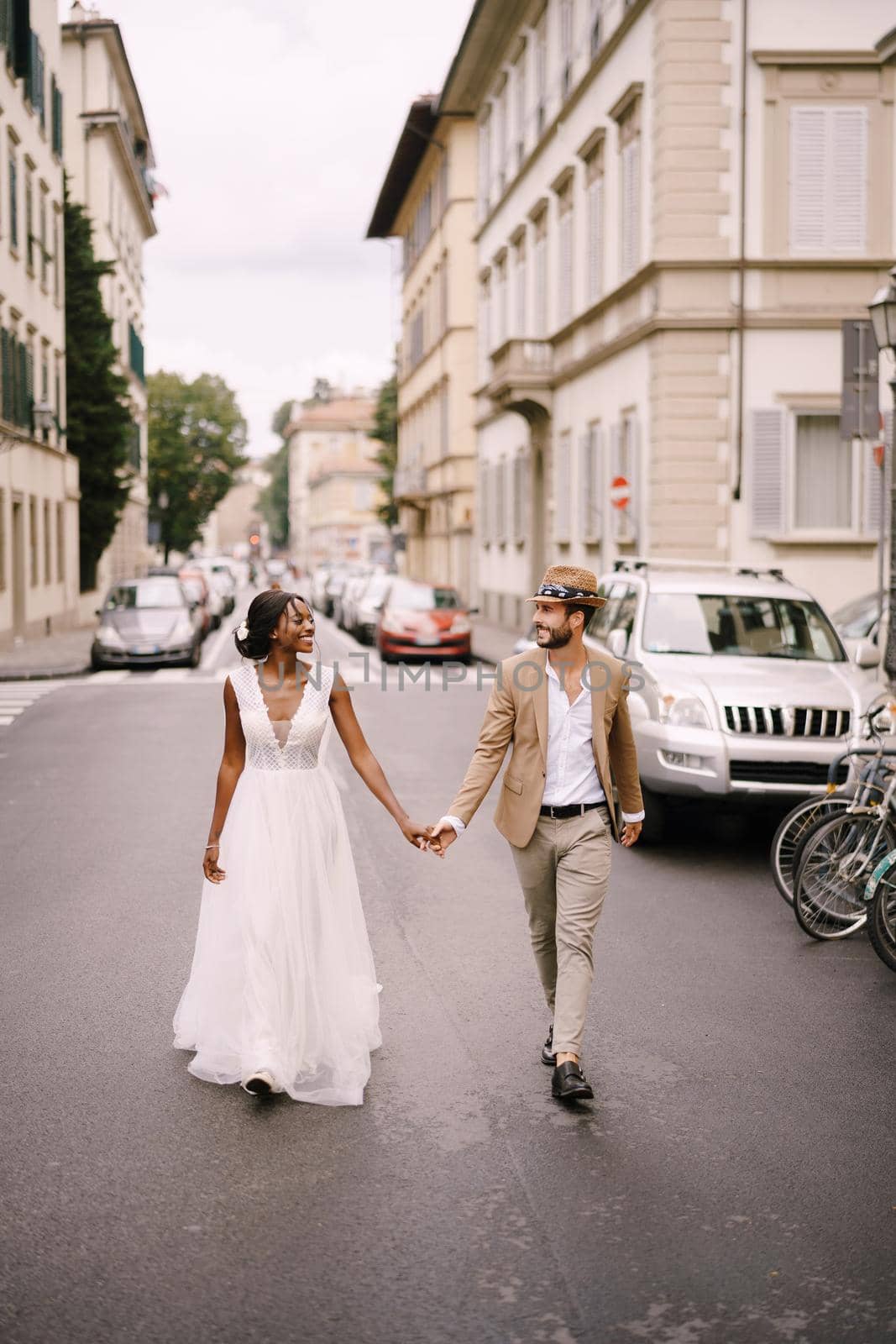 Wedding in Florence, Italy. Interracial wedding couple. African-American bride and Caucasian groom walk along the road among cars.