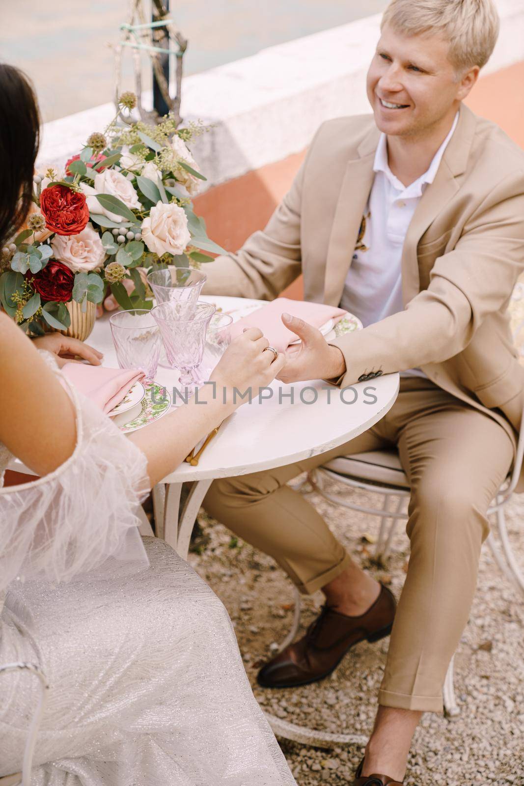 The bride and groom are sitting at tables on the banks of the Grand Canal and holding hands in Venice, Italy. The most romantic place on earth. Waiting for a romantic dinner for two, close-up. by Nadtochiy