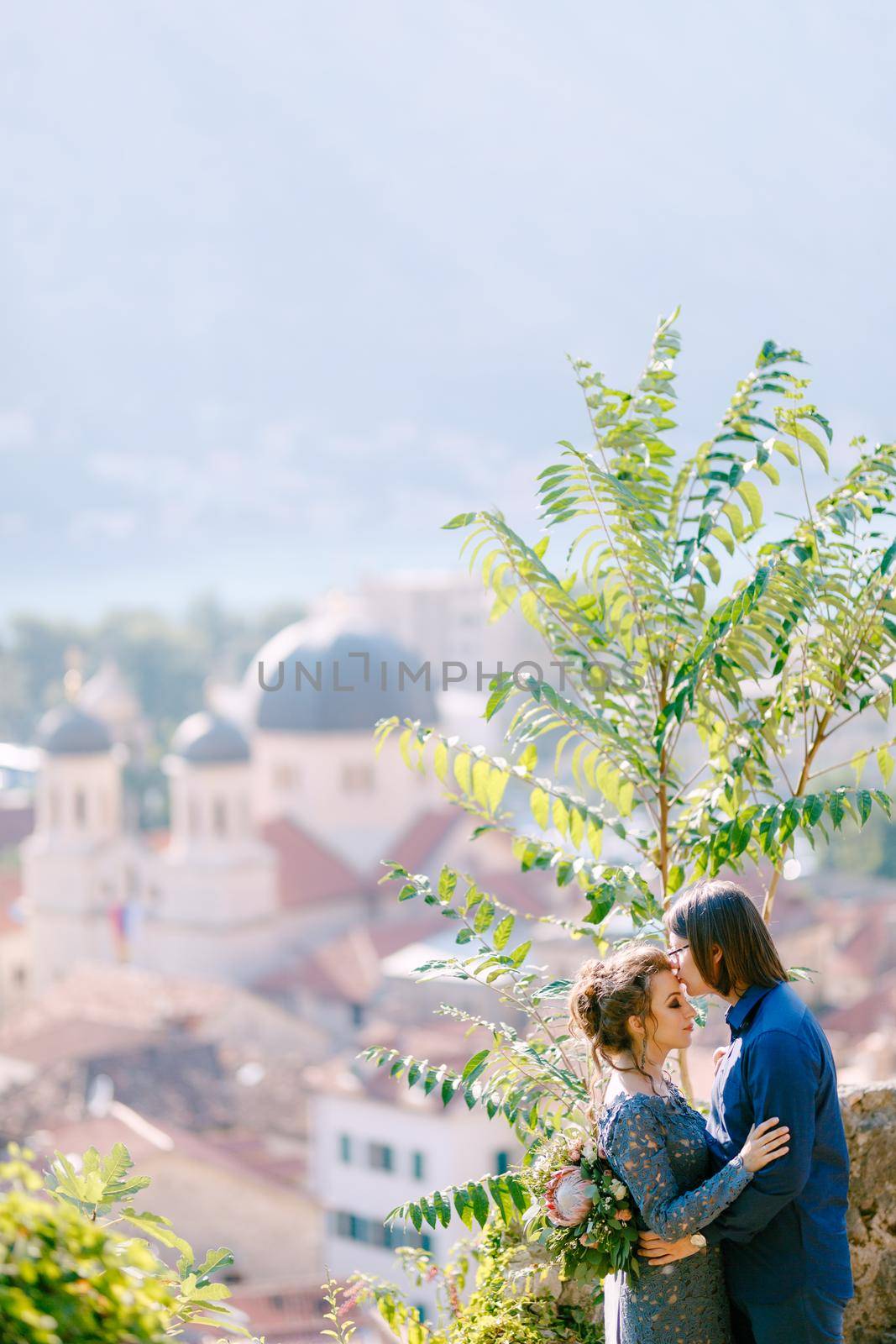 The bride and groom hug on the observation deck with a picturesque view of the old town of Kotor, close-up by Nadtochiy