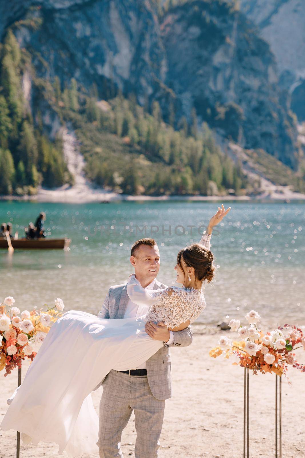 The groom circles the bride in her arms at the venue for the ceremony, with two autumn floral columns instead of an arch, against the backdrop of Lago di Braies in Italy