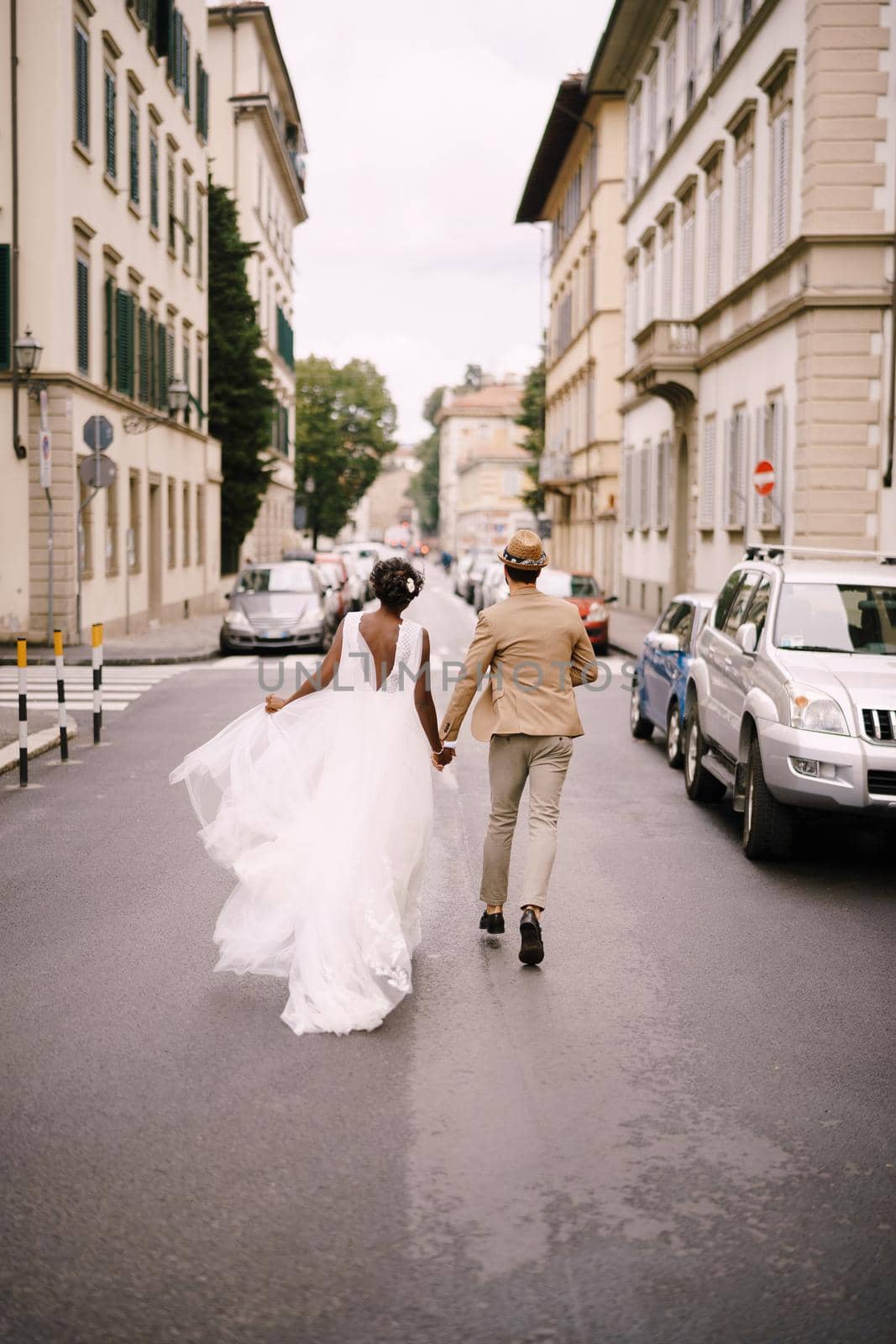 Wedding in Florence, Italy. Interracial wedding couple. African-American bride and Caucasian groom walk along the road among cars.