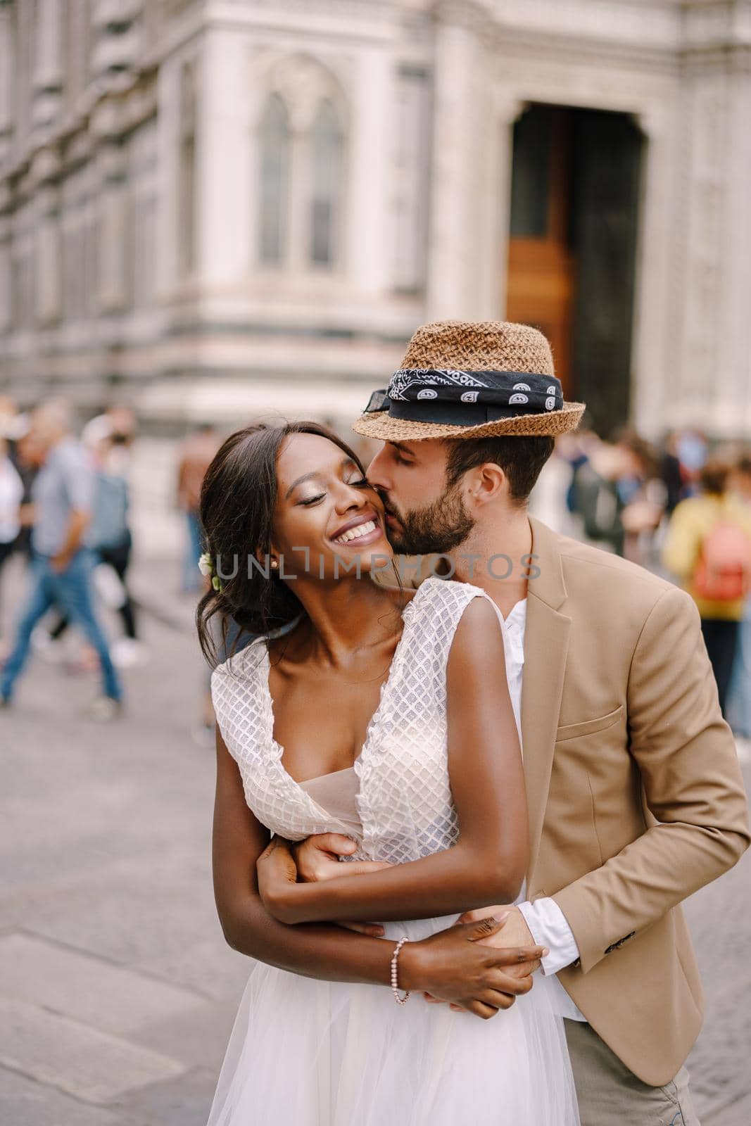 Caucasian groom hugs from behind and kisses African-American bride. Multiethnic wedding couple. Wedding in Florence, Italy.