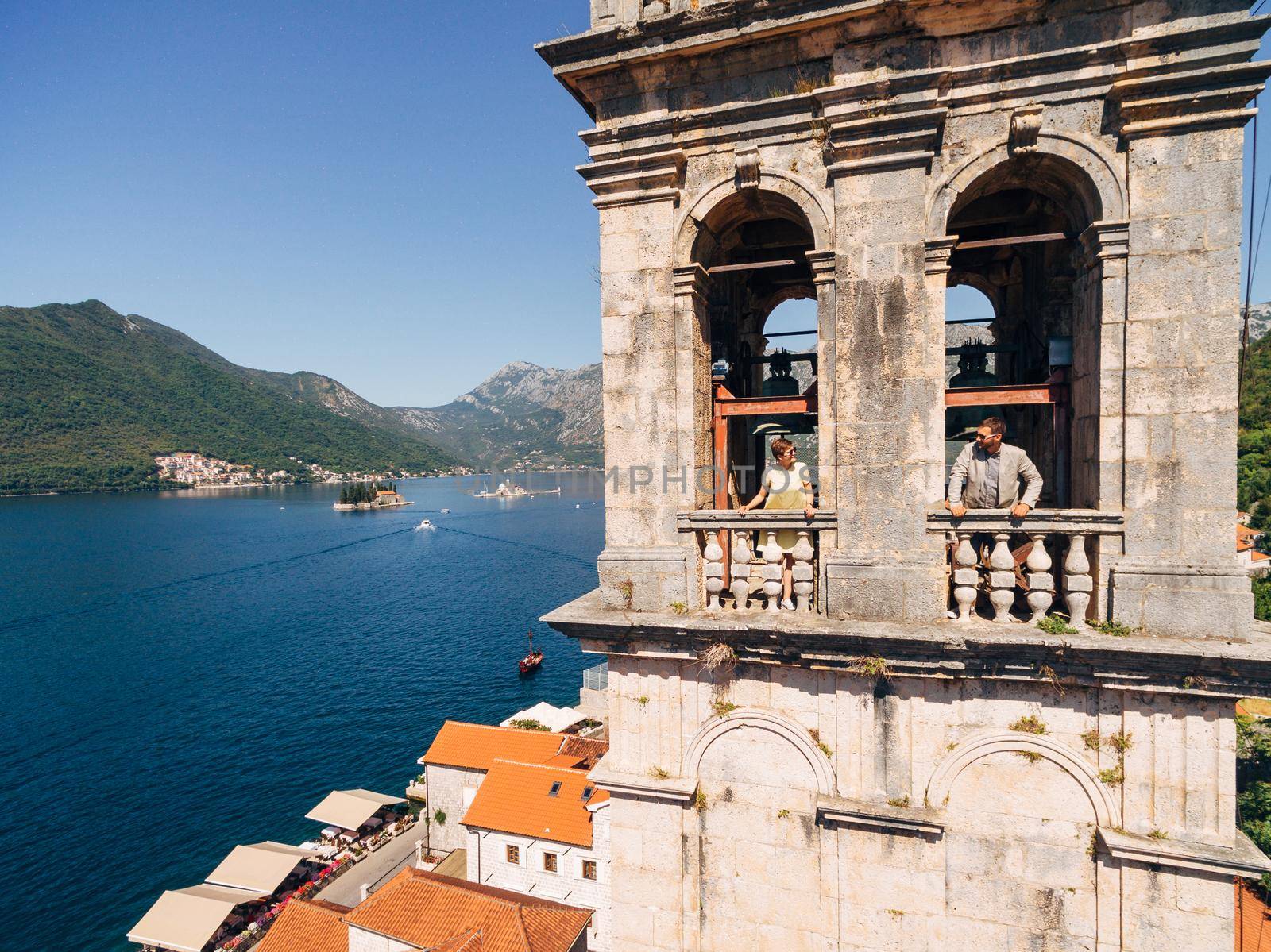 A man and a woman look out of the windows of the tower and look at each other over the old town of Perast . High quality photo