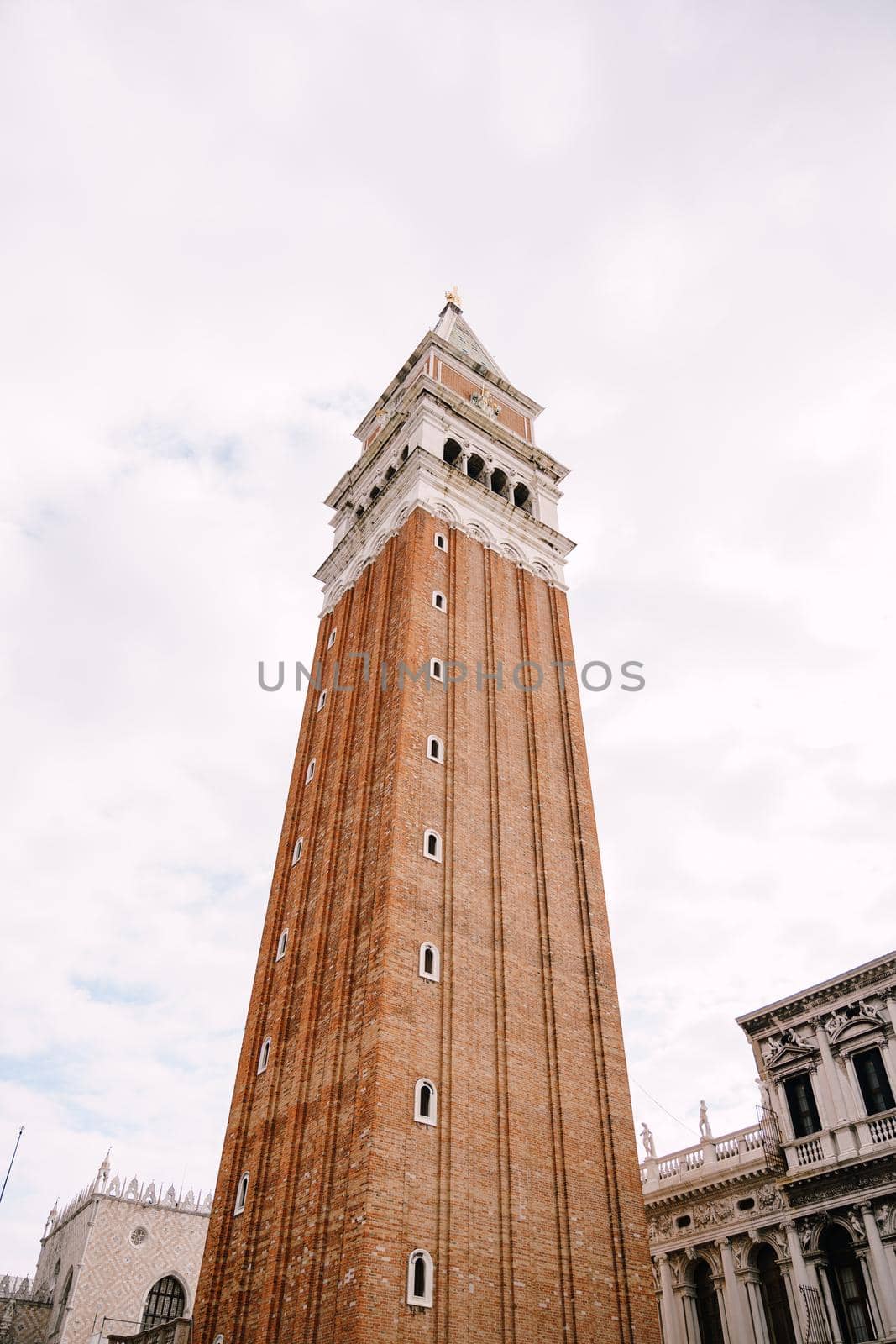 A huge bell tower made of red brick in Piazza San Marco in Venice, Italy. Against background of a cloudy, evening, October sunset sky.
