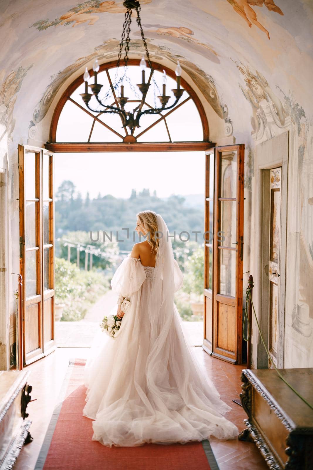 Wedding at an old winery villa in Tuscany, Italy. The bride walks in the interior of the villa, overlooking the garden. by Nadtochiy