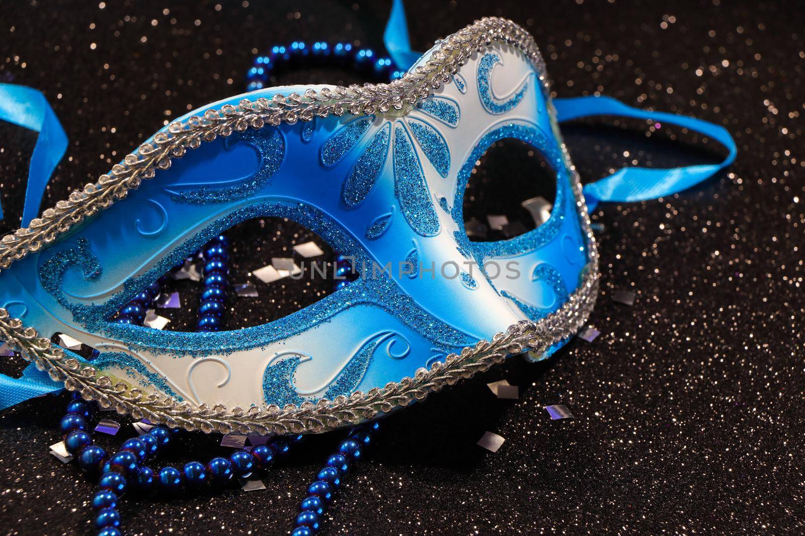 Mardi Gras blue carnival face mask with bead string and silver confetti on textured black